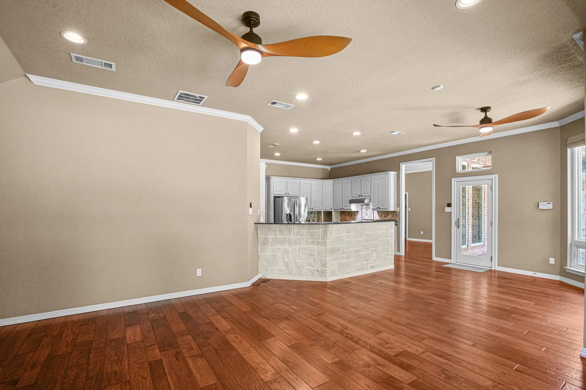 Wood-finish flooring, crown molding, recessed lighting, ceiling fans, and a stone-clad breakfast bar