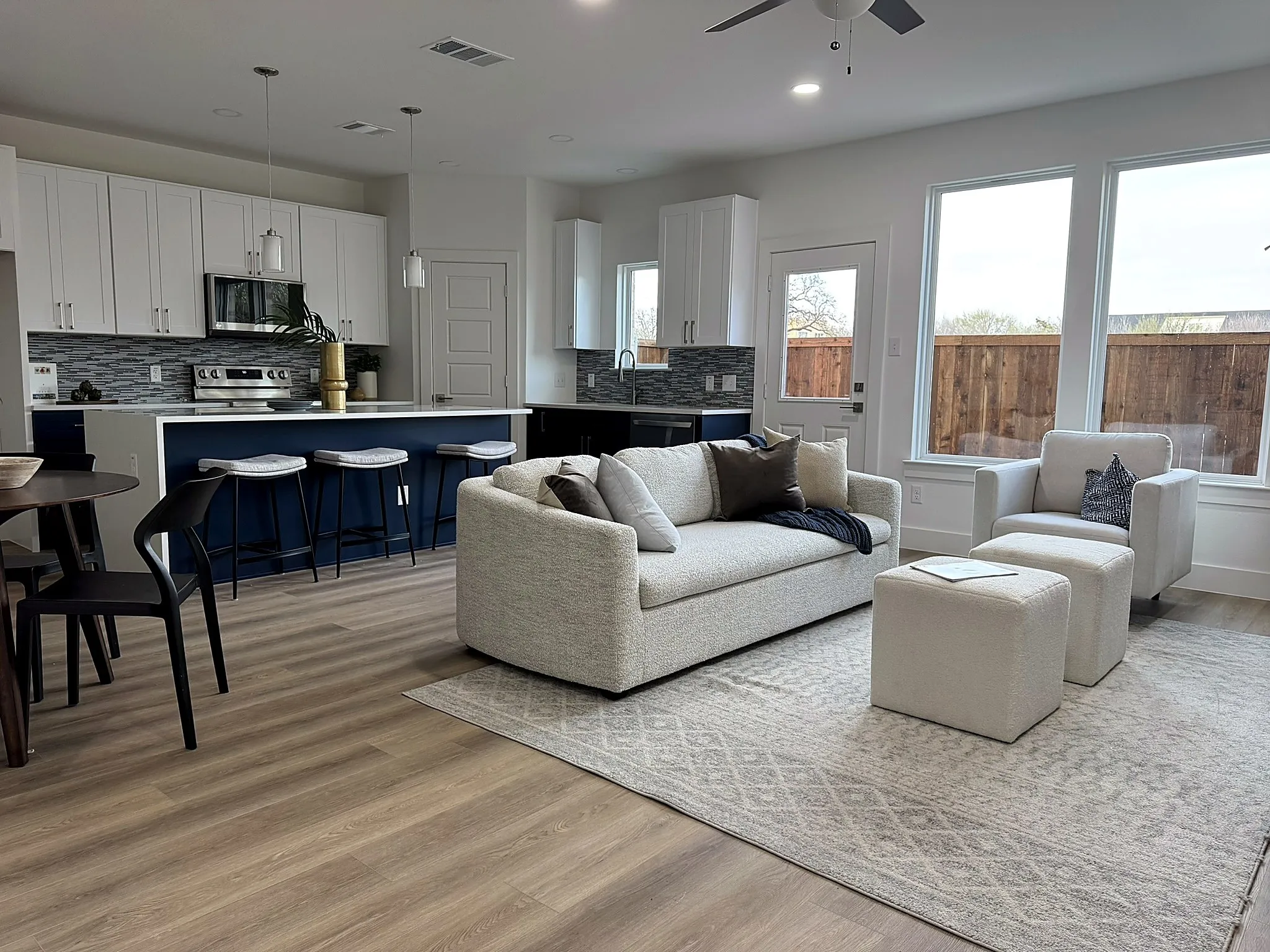Open-concept living area with wood-finish flooring, white cabinetry, a kitchen island with seating, and a ceiling fan