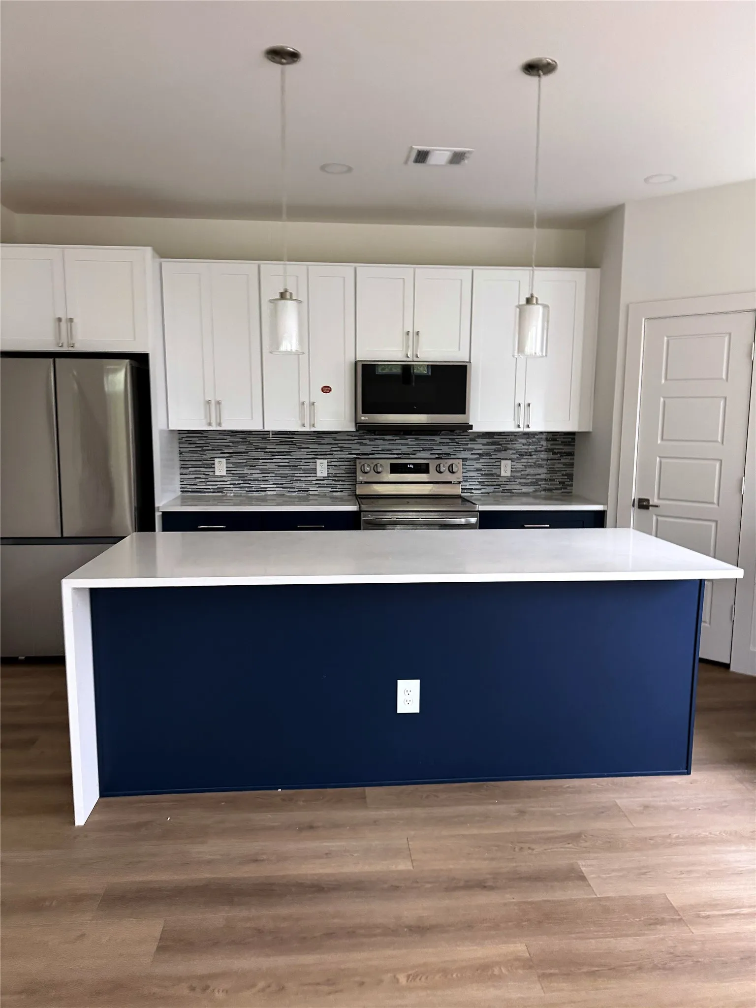 Kitchen featuring a large island with a waterfall countertop, pendant lighting, stainless steel appliances, and wood-finish flooring