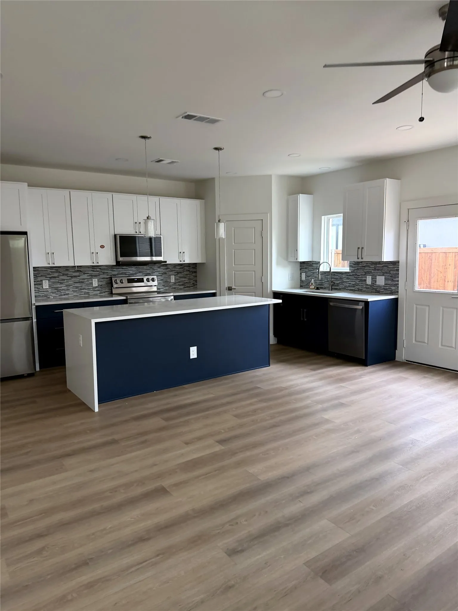 Open-concept kitchen featuring an island with a white countertop, two-tone cabinetry, stainless steel appliances, and wood-finish flooring