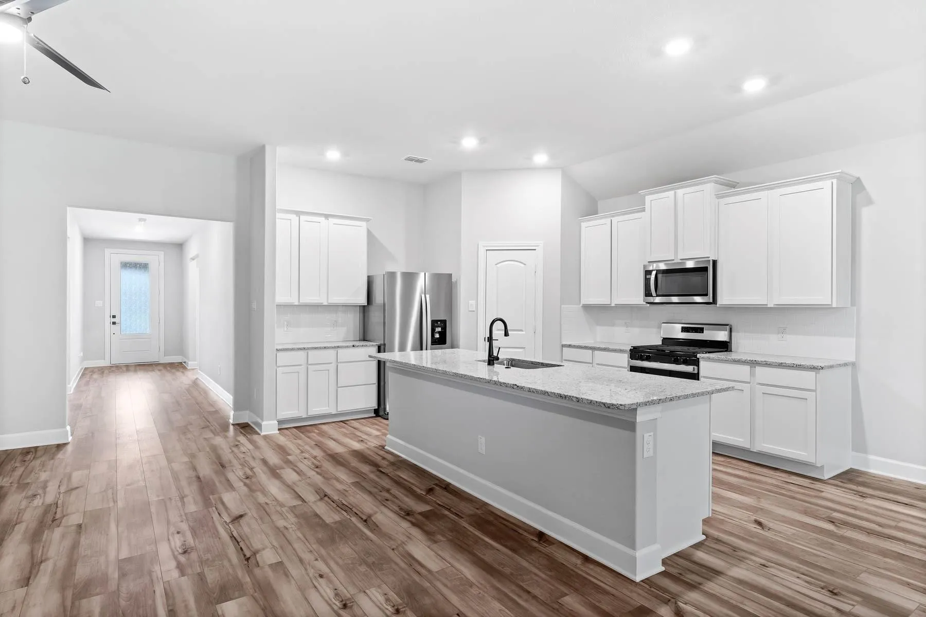 Kitchen featuring white cabinetry, appliances with stainless steel finishes, an island with sink, light stone countertops, and recessed lighting