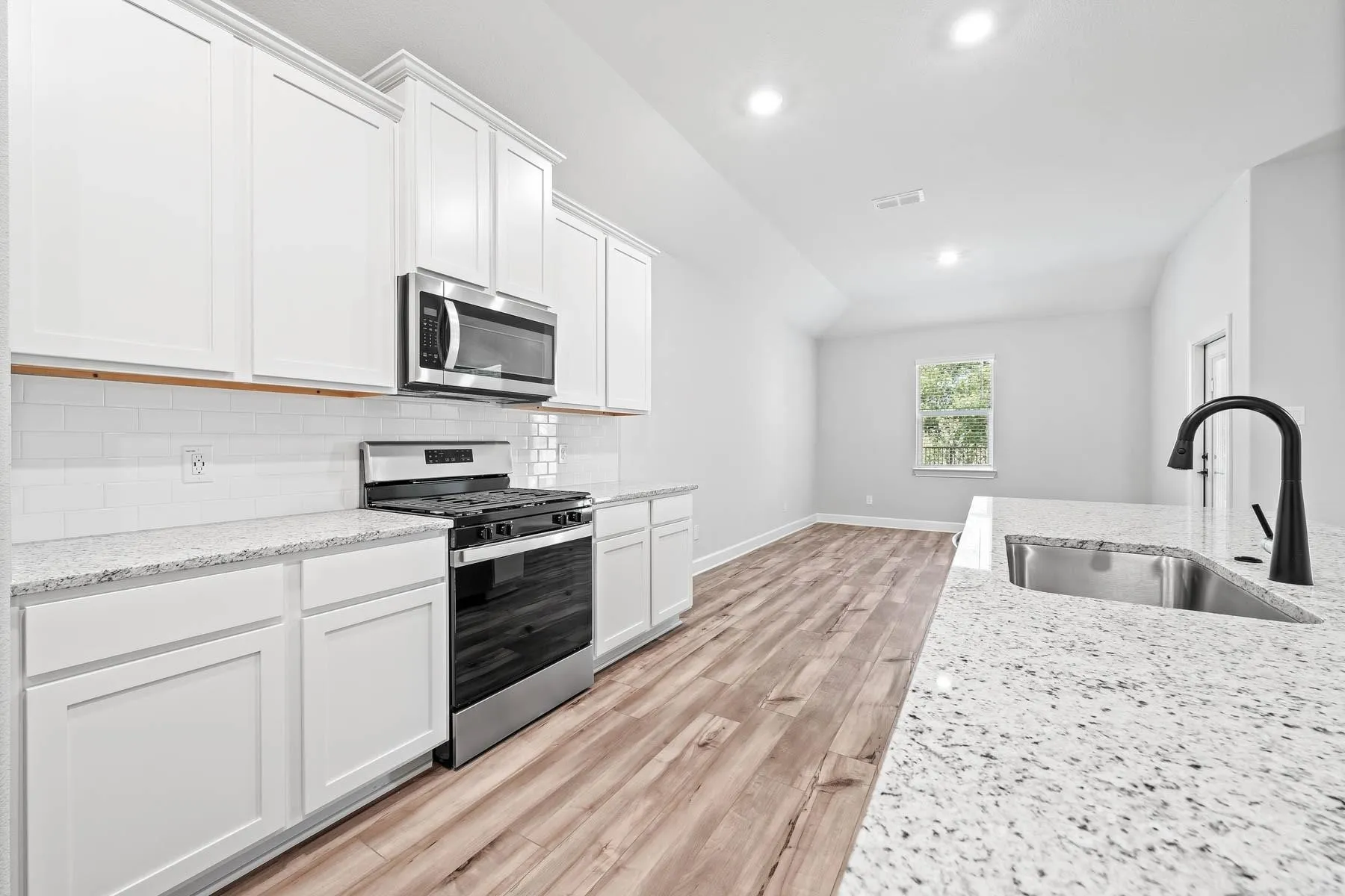 Kitchen featuring appliances with stainless steel finishes, white cabinets, tasteful backsplash, light stone counters, and recessed lighting