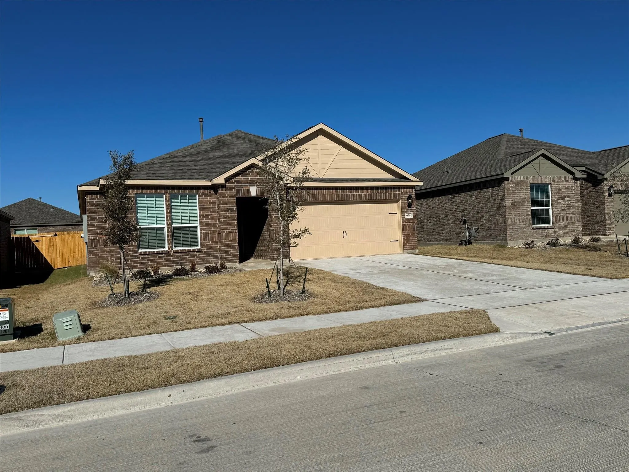 Single story home featuring driveway, brick siding, an attached garage, and roof with shingles