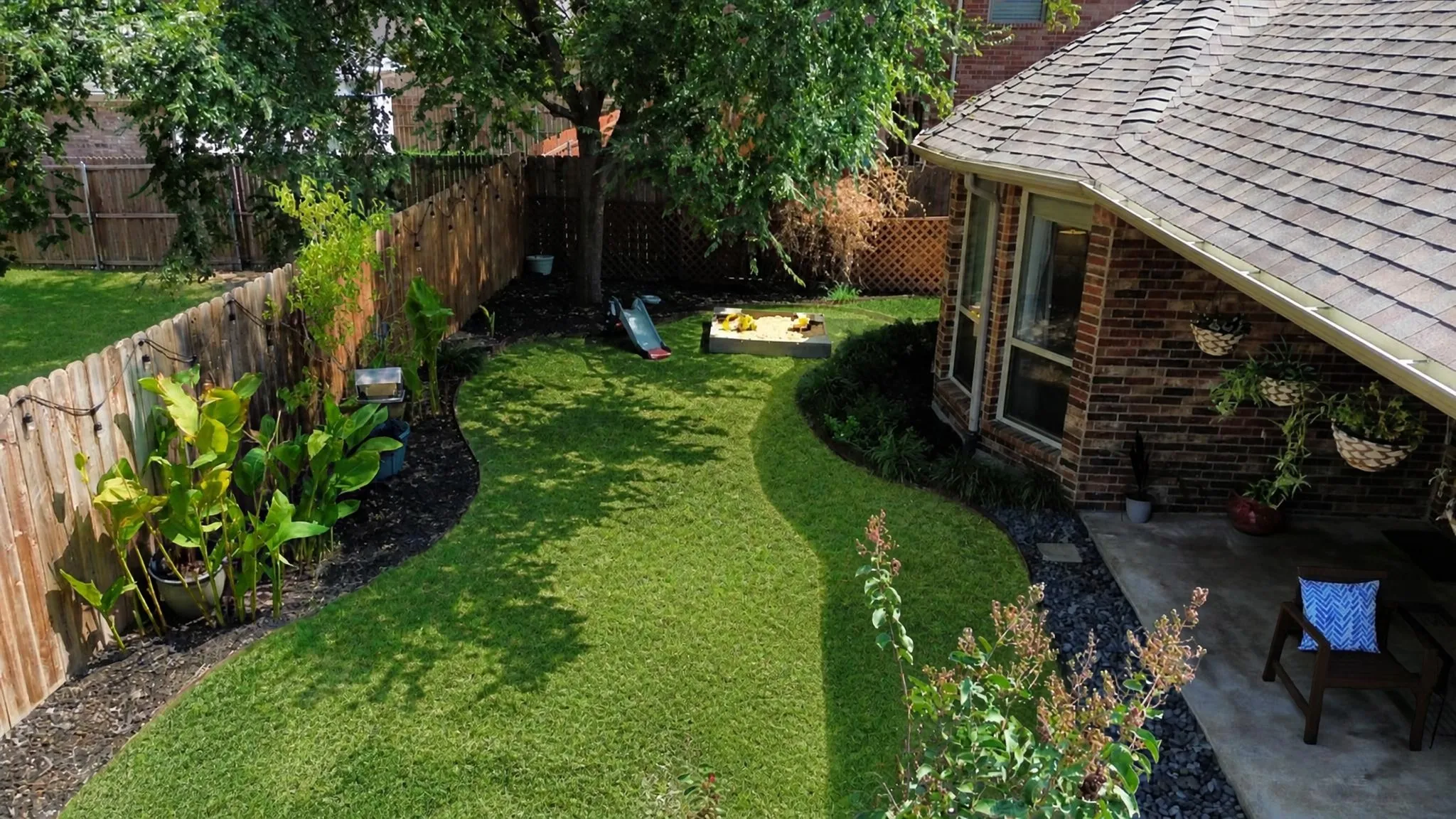 Manicured backyard with a curved lawn, mature trees, and a brick exterior
