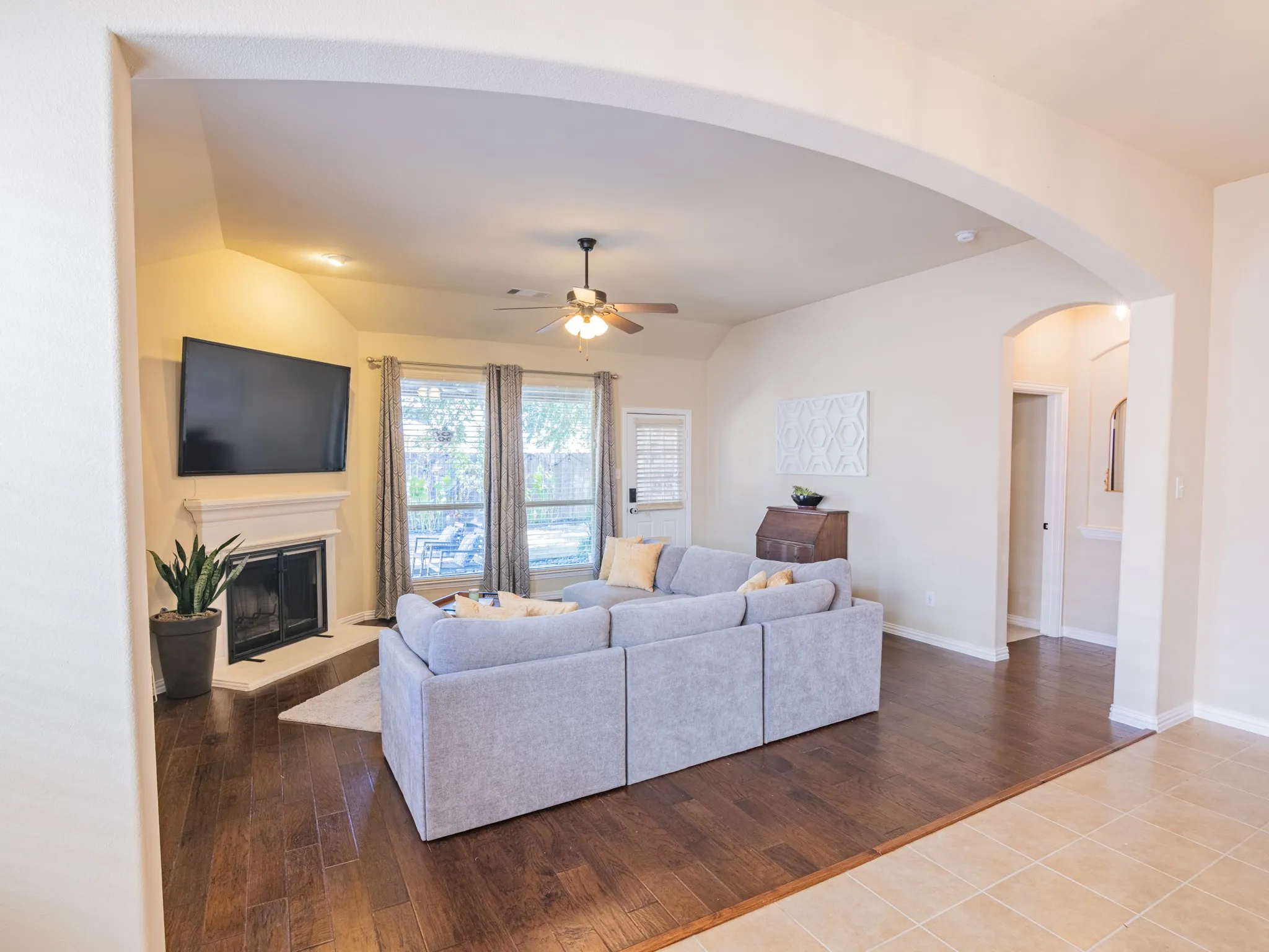 Vaulted ceiling, wood-finish flooring, fireplace with mantel, ceiling fan, and large windows