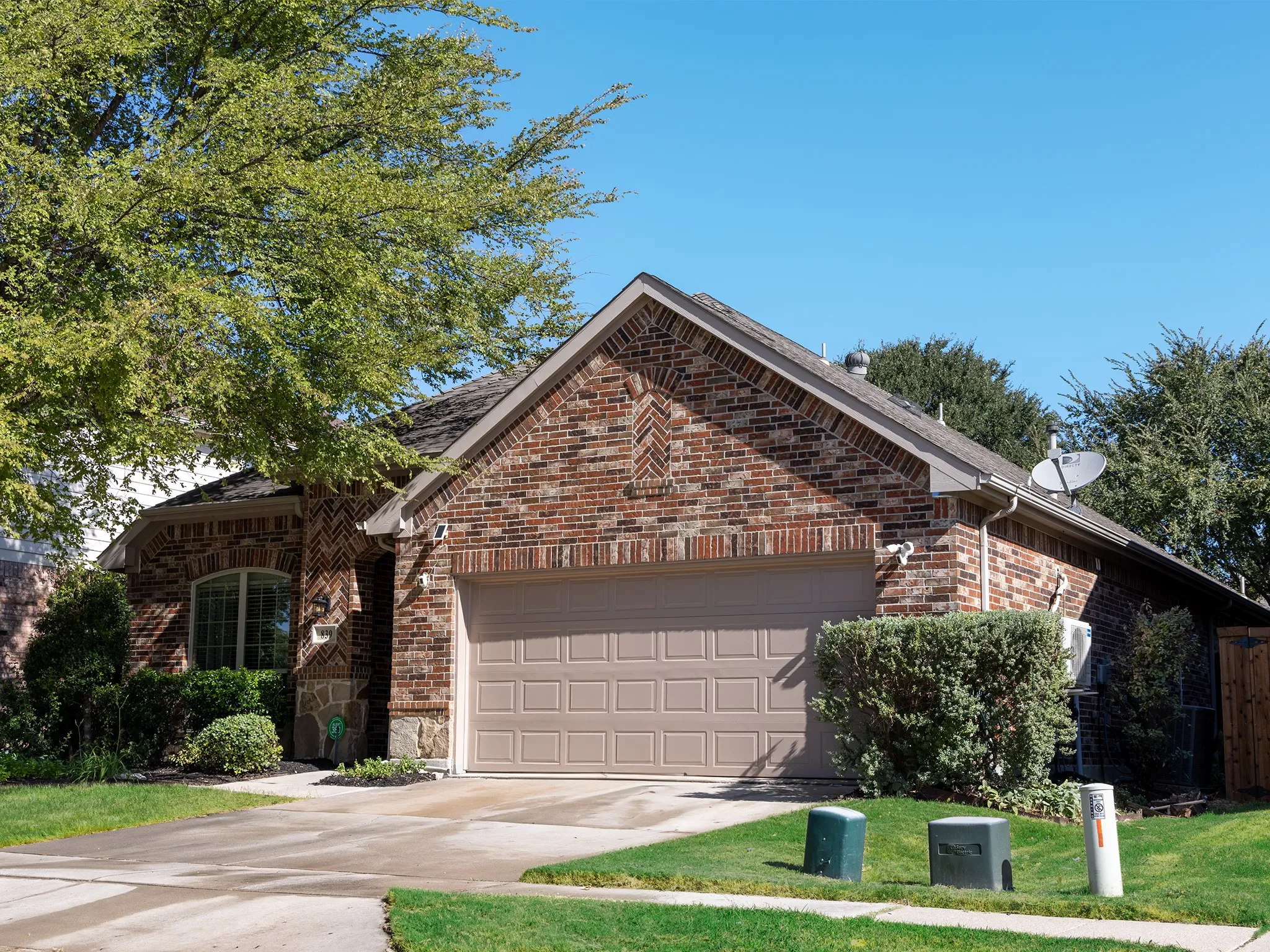 Brick exterior with stone accents, attached garage, arched window, and mature landscaping