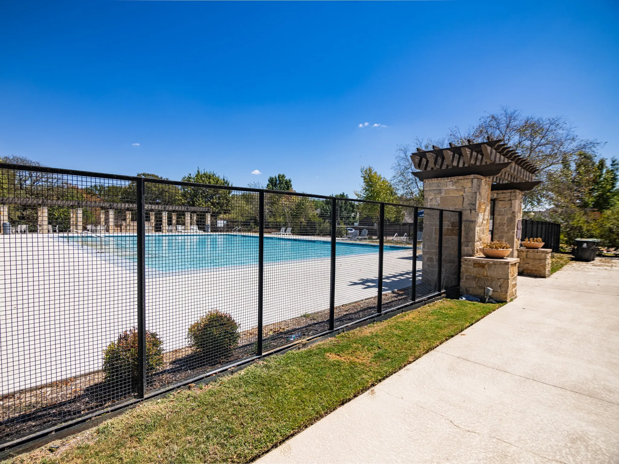 Community swimming pool with a stone pillar entryway, paved decking, and perimeter fencing