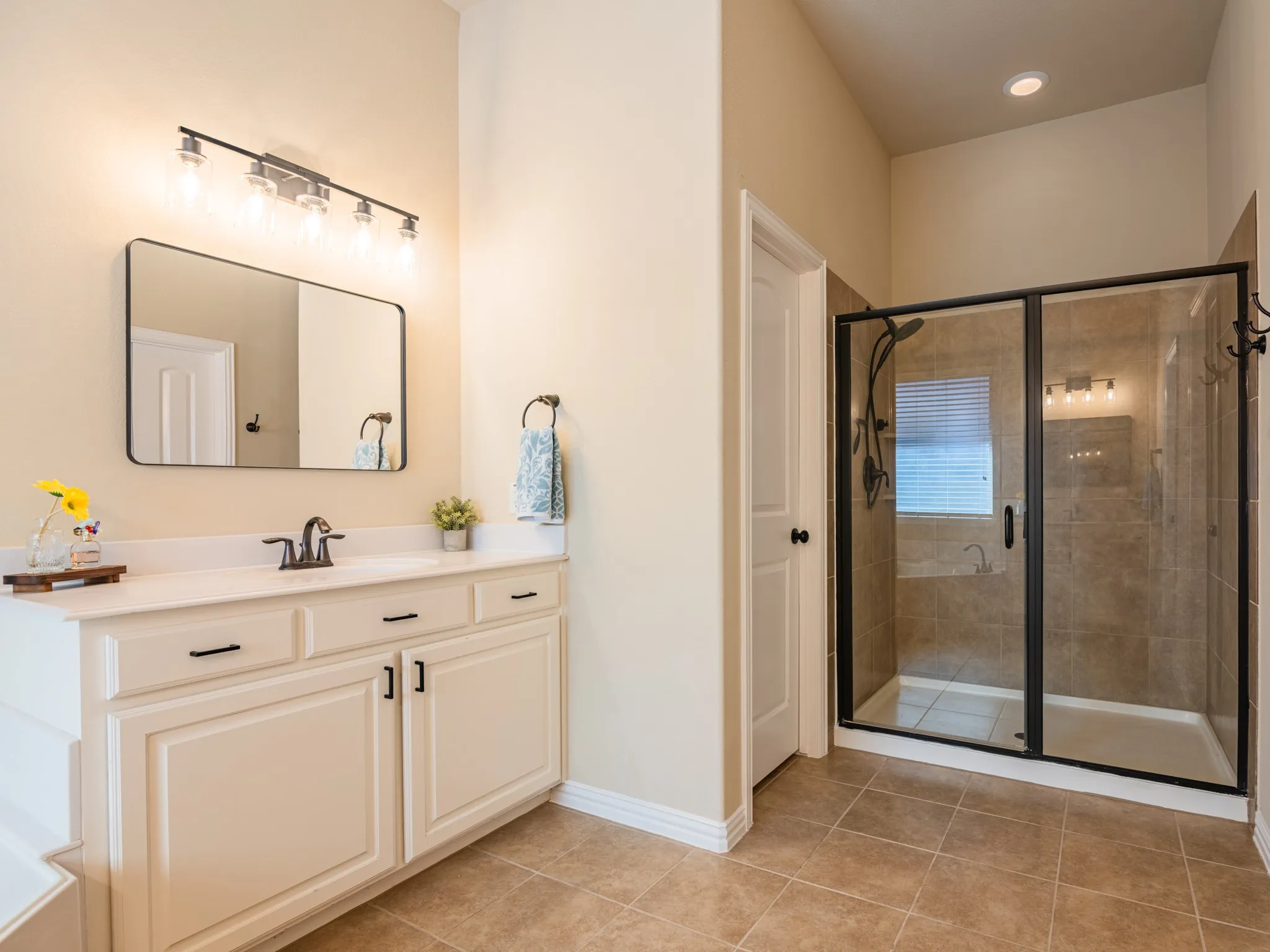 Spacious bathroom featuring a single vanity with a white countertop, recessed lighting, a walk-in shower with a glass enclosure, and tiled flooring