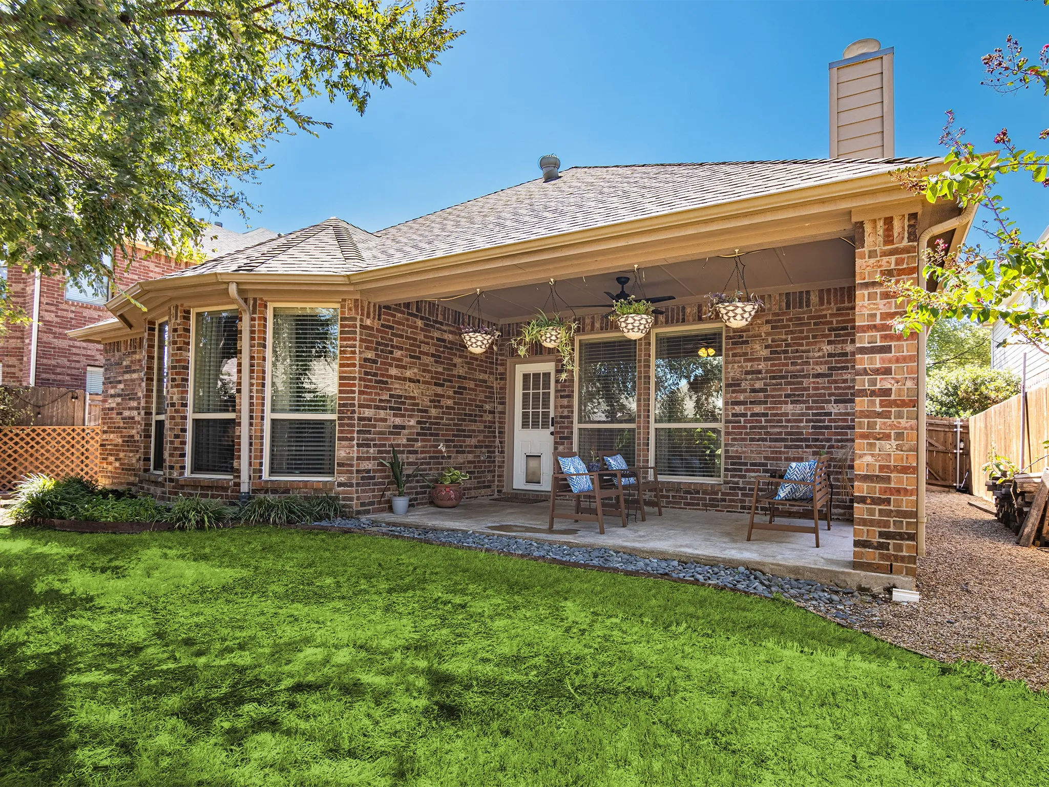 Brick exterior with a covered patio, multiple large windows, and a shingle roof
