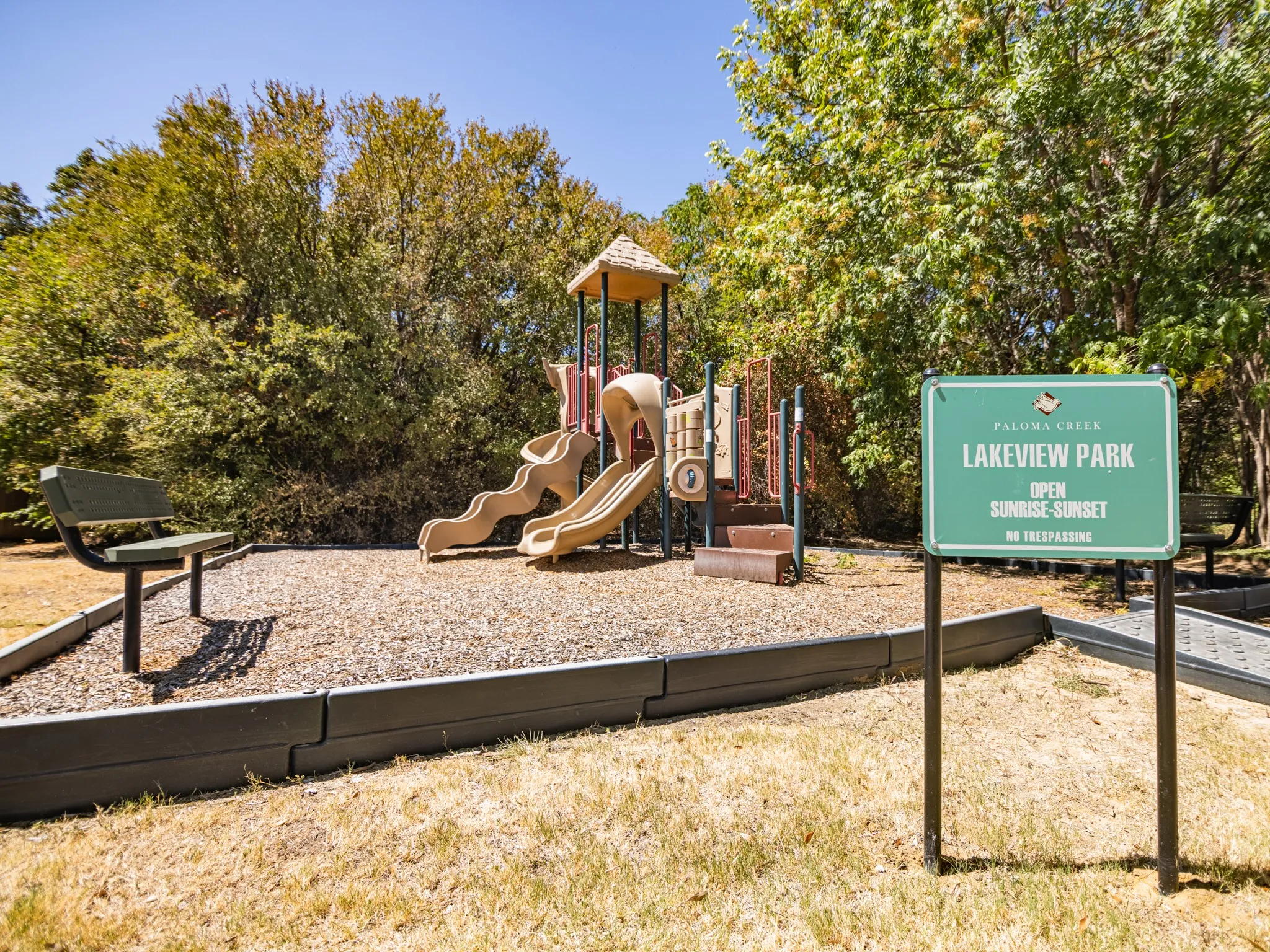 Playground area featuring a multi-level play structure with slides, a park bench, and a sign identifying the area as Lakeview Park