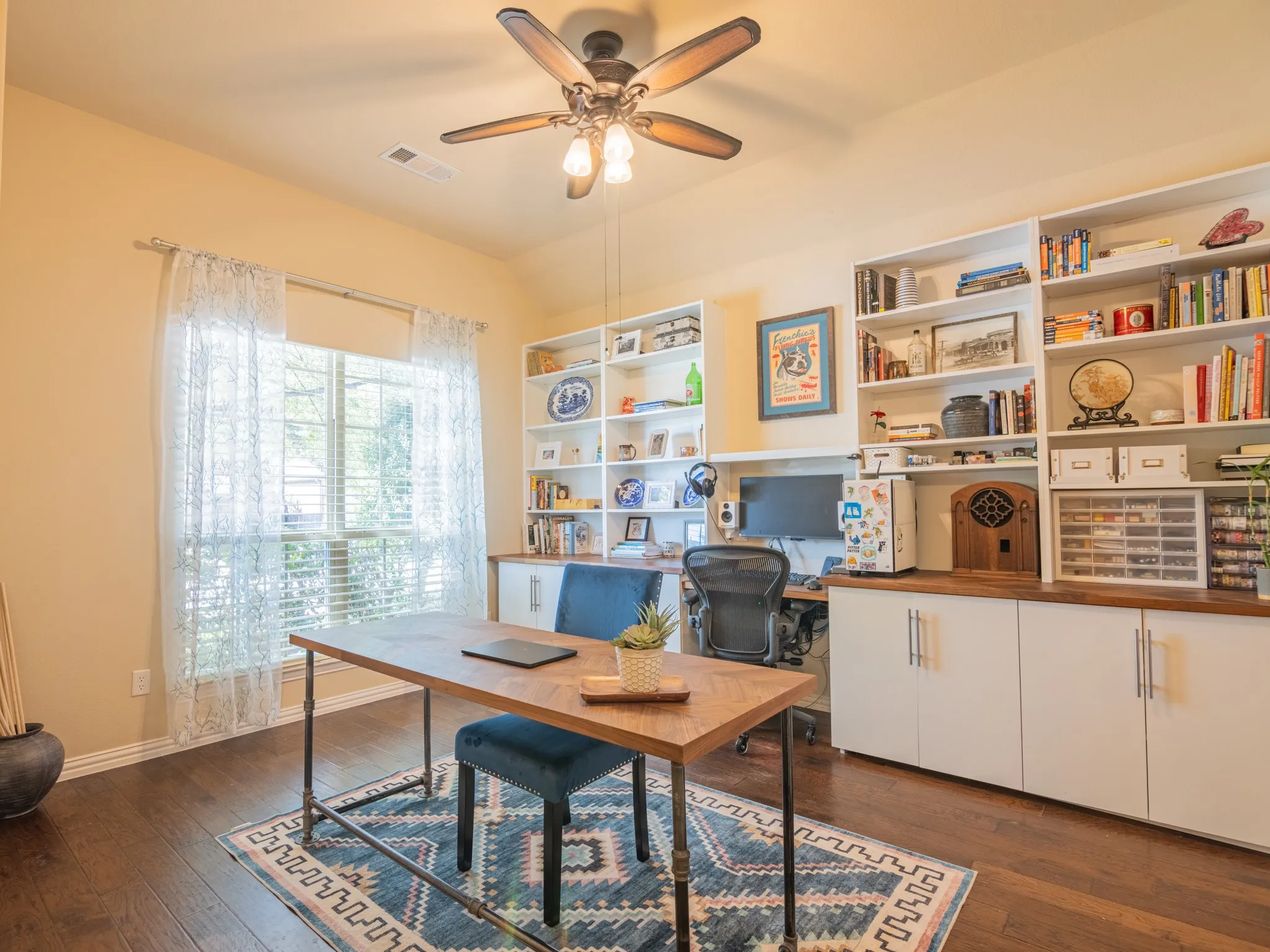 Hardwood flooring, custom built-in shelving, a ceiling fan with integrated lighting, and a window with blinds