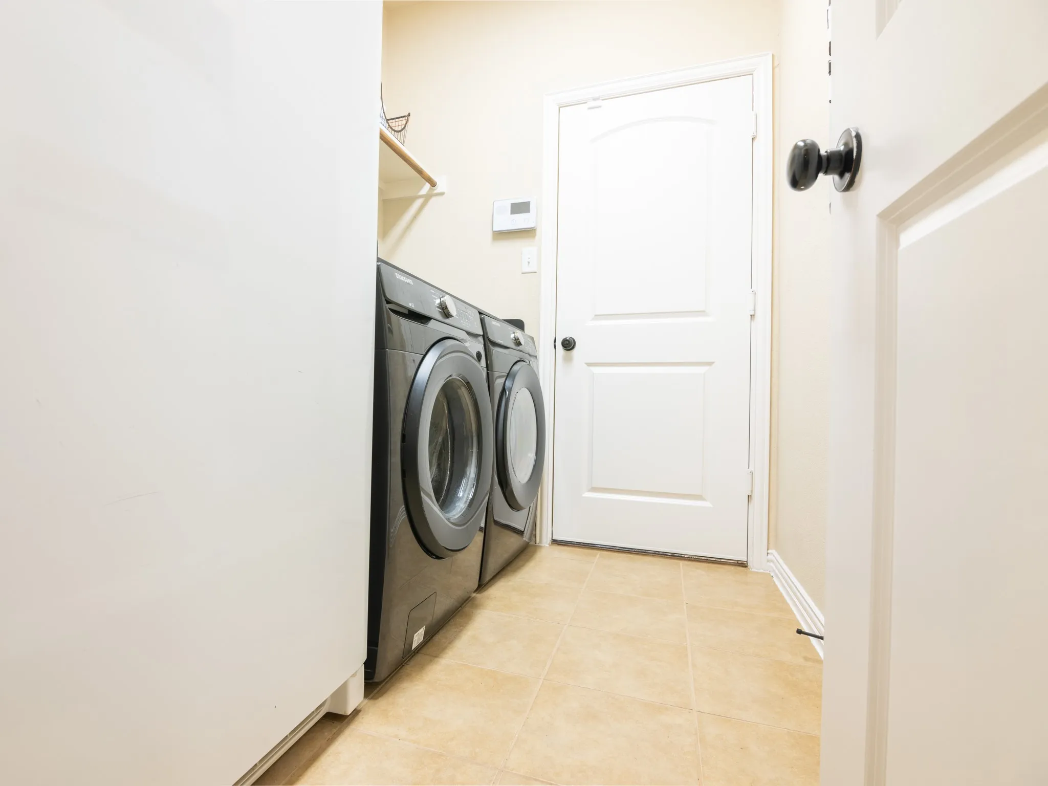 Laundry area featuring neutral tile flooring and a built-in wall shelf