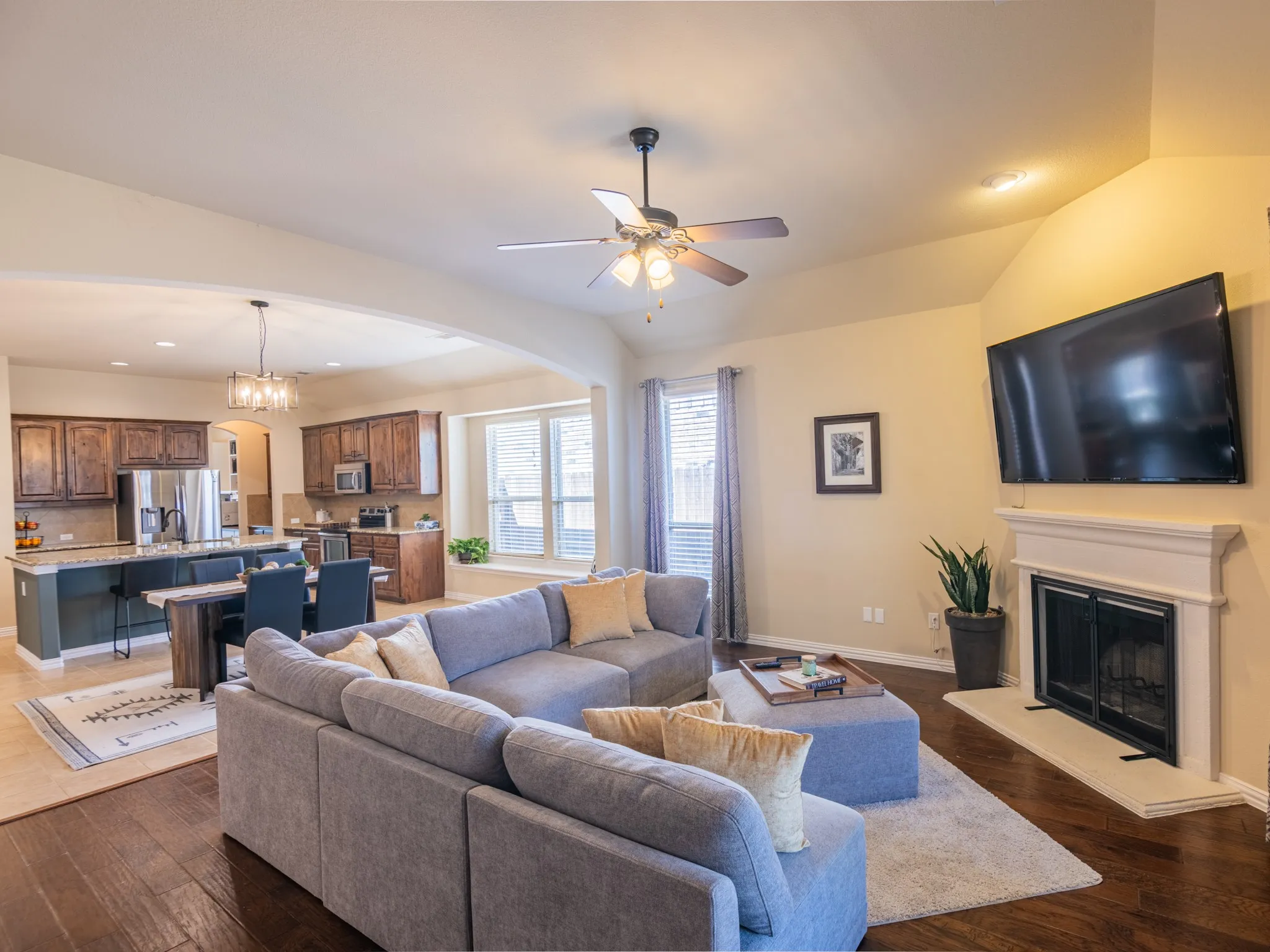 Open-concept living space featuring wood-finish flooring, a vaulted ceiling with a ceiling fan, and a fireplace with a mantel