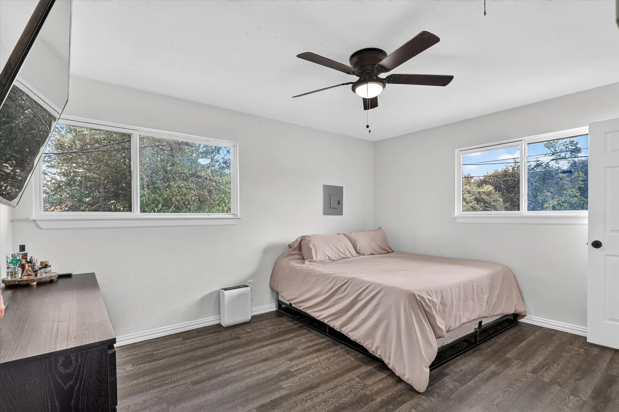 Wood-finish flooring, white walls, two windows, and a ceiling fan with integrated lighting