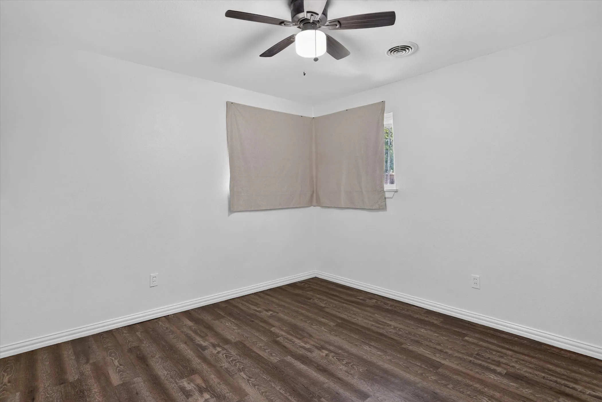 Wood-finish flooring, white walls, ceiling fan with integrated lighting, and a single window