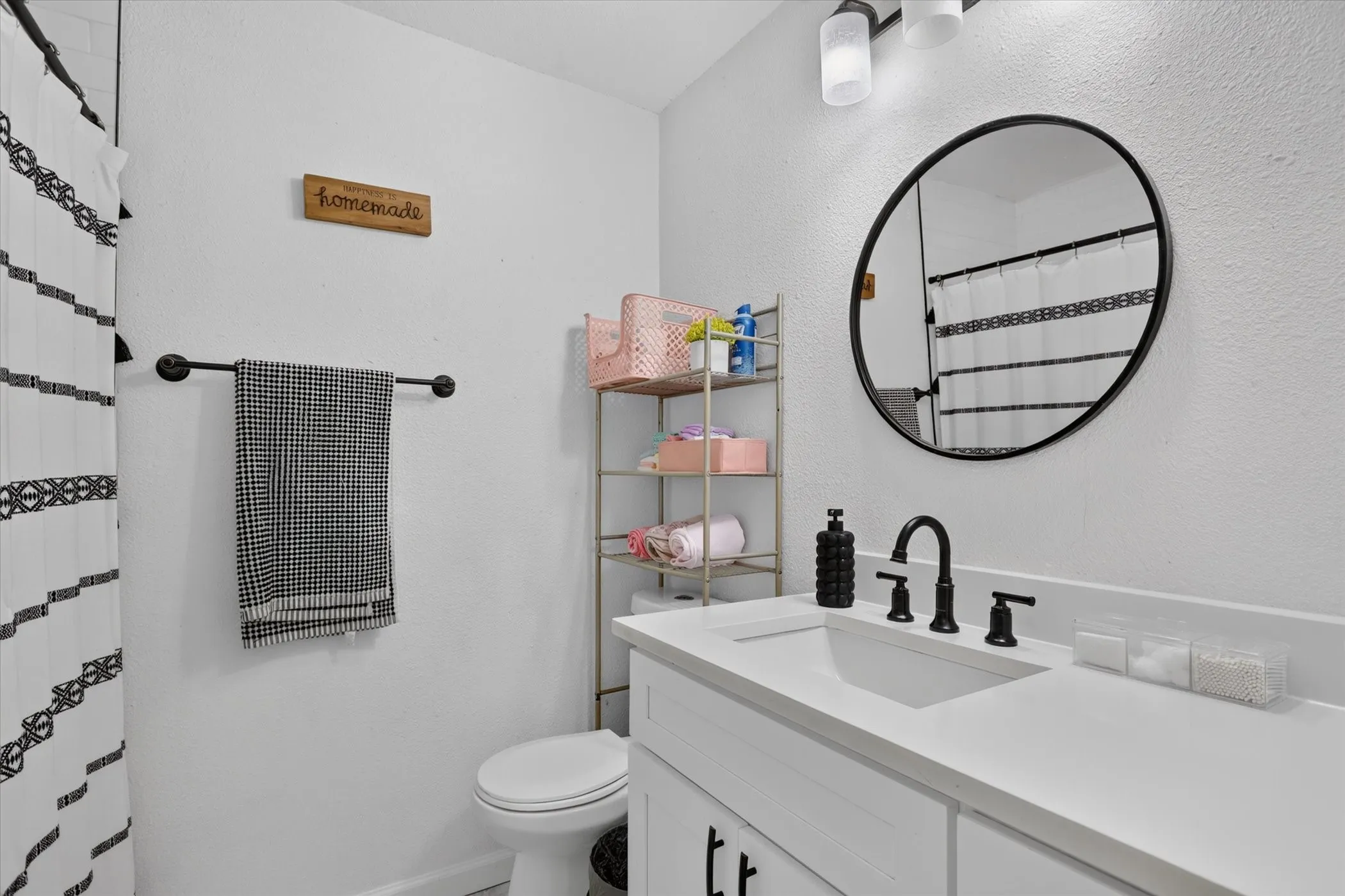 White vanity with a rectangular undermount sink, a matte black faucet, and a round black-framed mirror