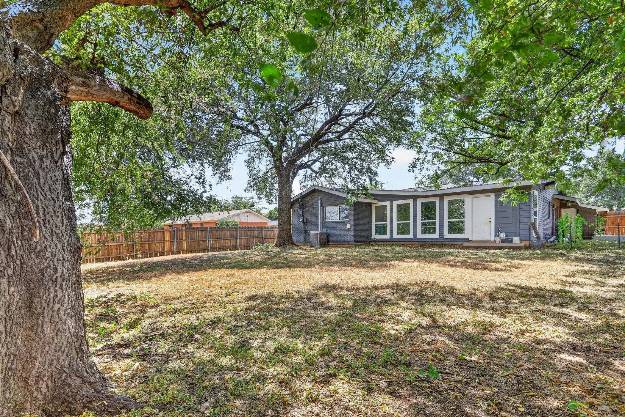 Expansive backyard with mature trees, a privacy fence, and a gray-painted exterior