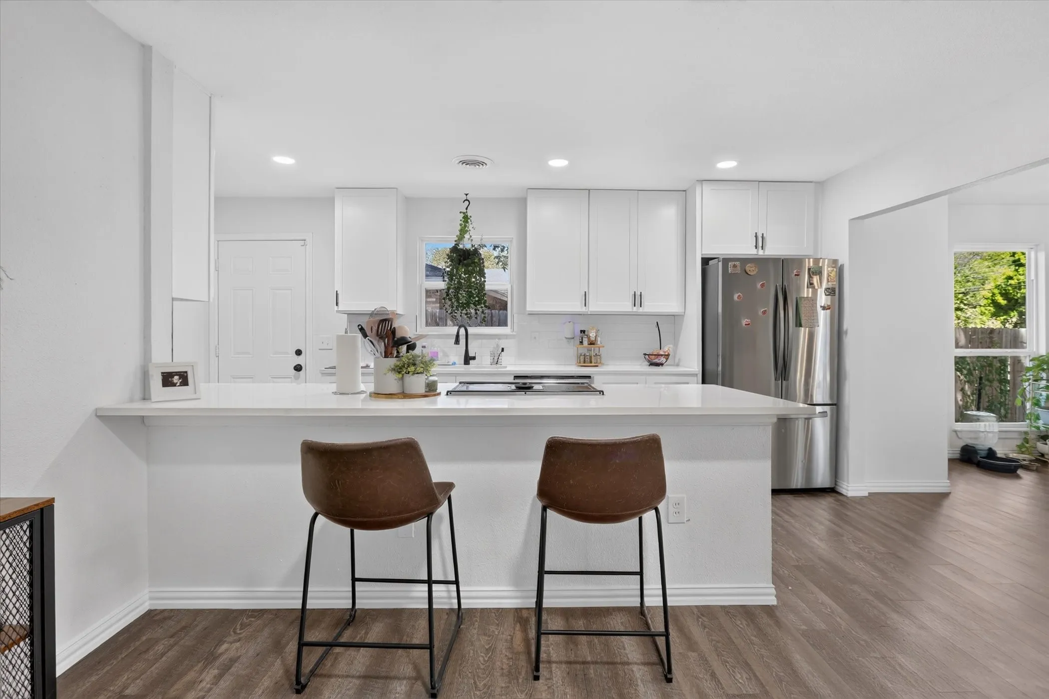 Kitchen with white cabinetry, stainless steel refrigerator, white countertops, and wood-finish flooring