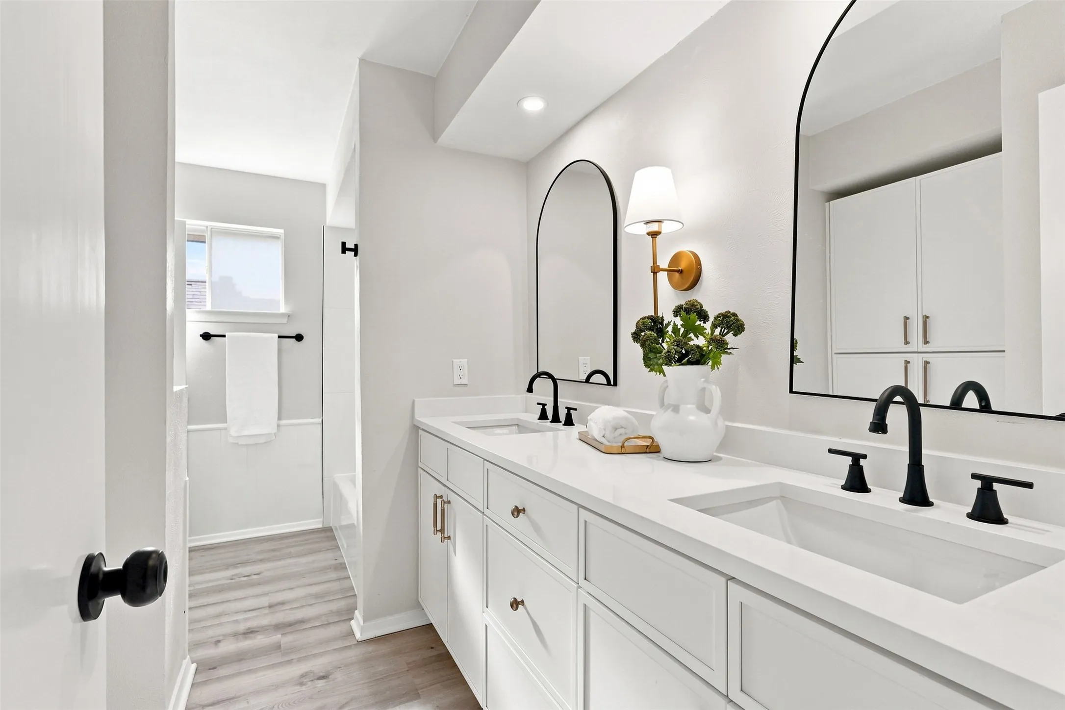 Dual vanity with integrated sinks, matte black fixtures, arched mirrors, built-in cabinetry, and wood-finish flooring