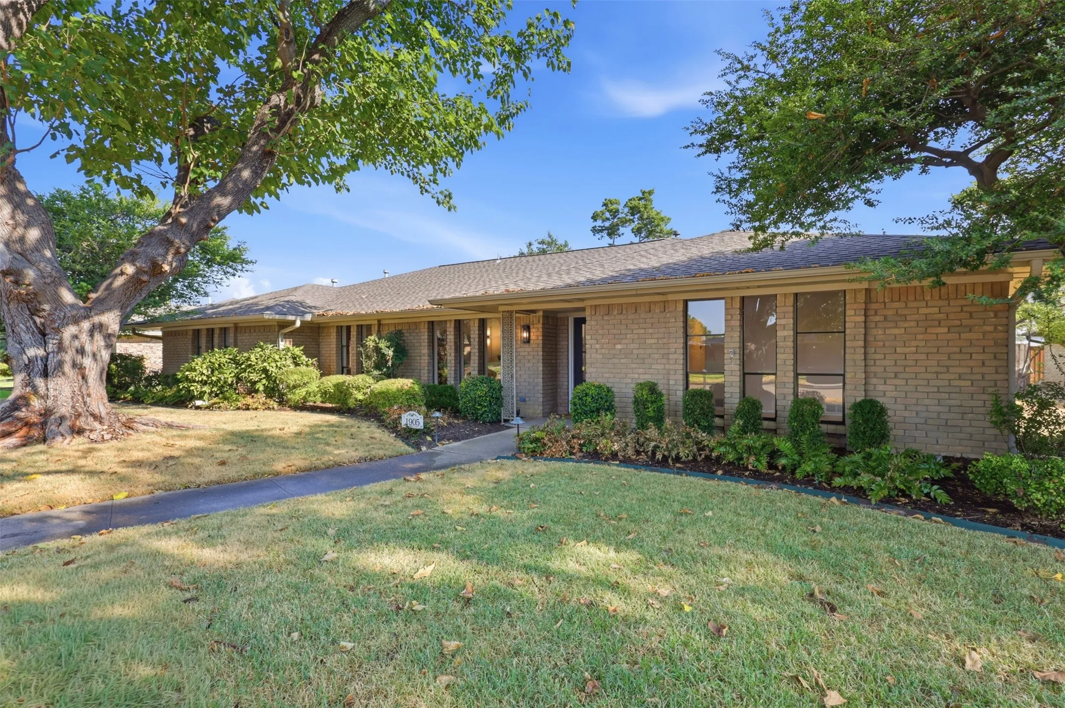 Brick facade residence with a gabled roofline, mature trees, and a concrete pathway