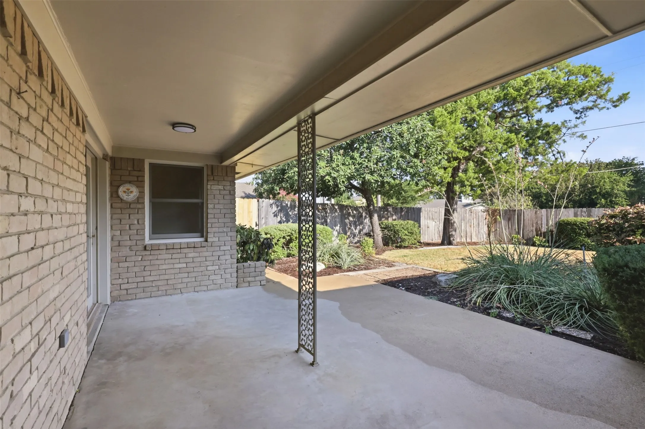 Covered concrete patio featuring a decorative metal support column and brick exterior wall