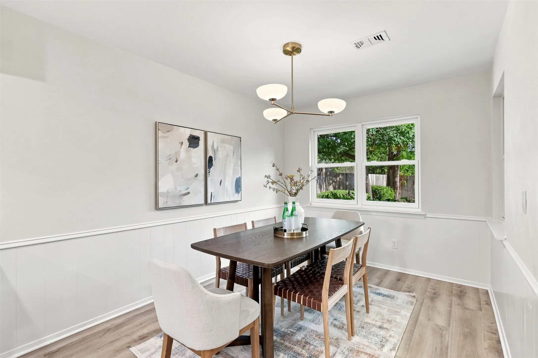 Wood-finish flooring, white paneled wainscoting, white walls, and a multi-globe chandelier
