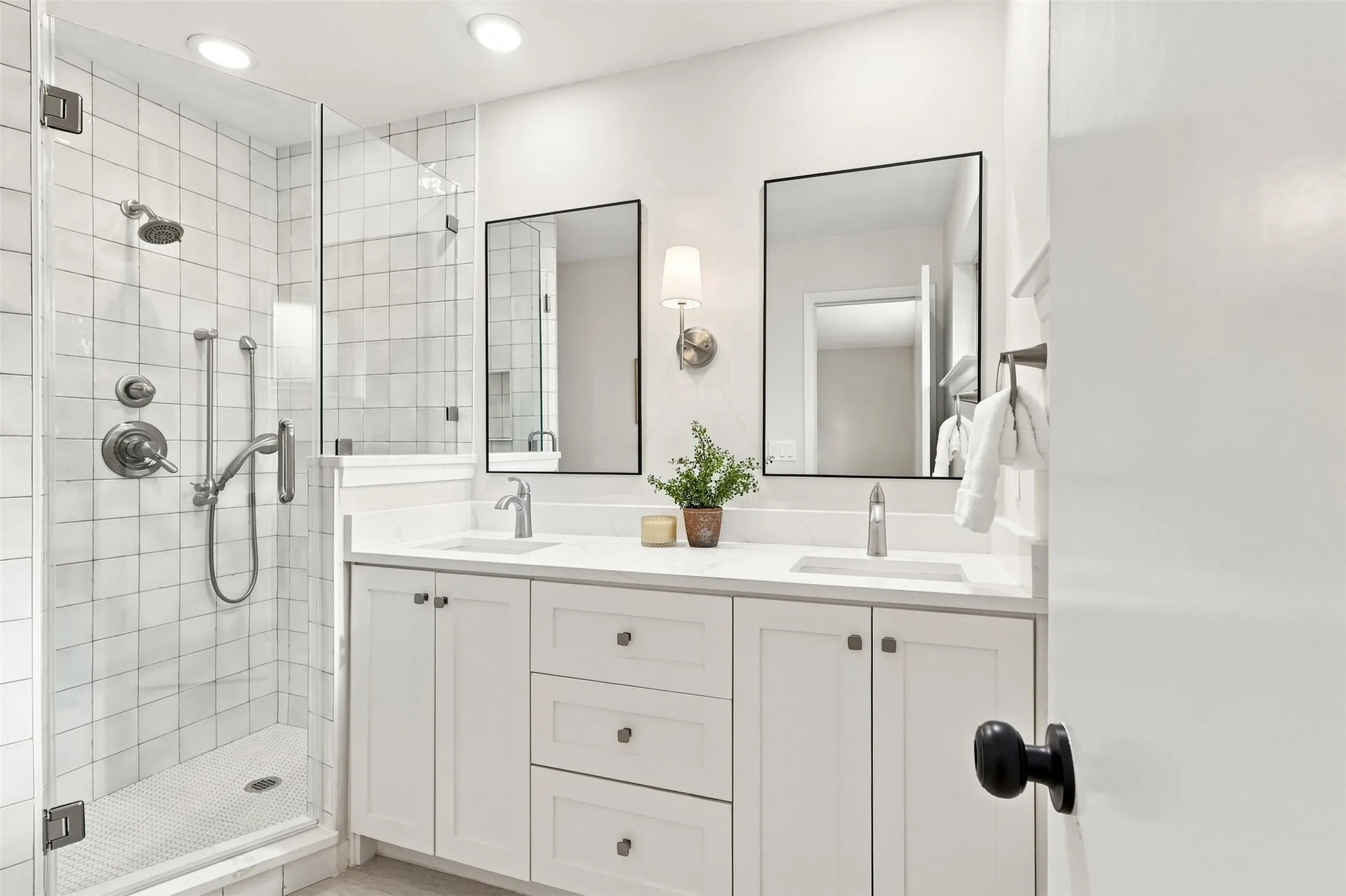 Glass-enclosed shower with subway tile surround, dual vanity with white cabinetry, quartz-finish countertops, and dual framed mirrors