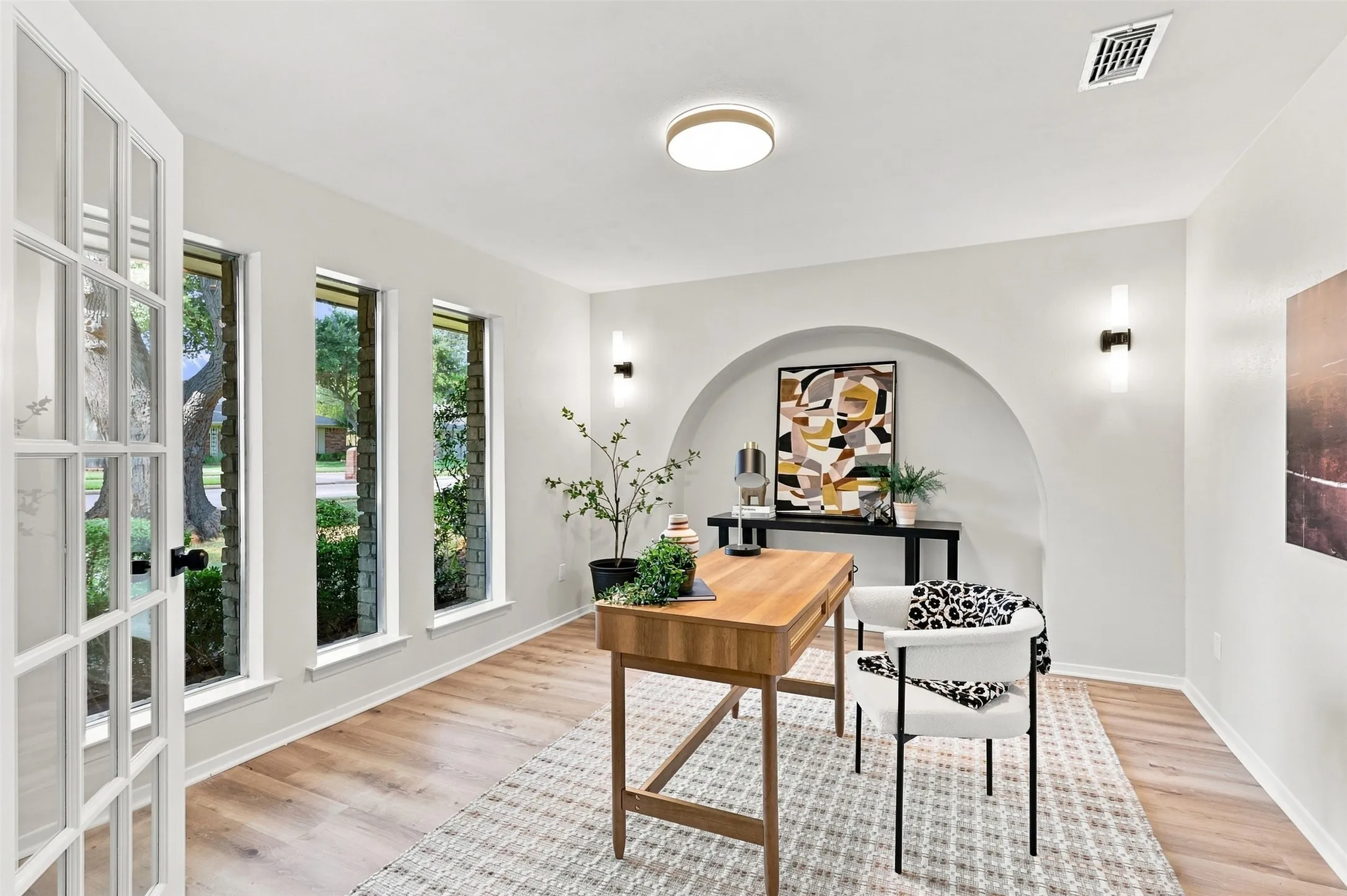 French doors with grid panels, multiple large windows, wood-finish flooring, recessed archway, and wall-mounted light fixtures