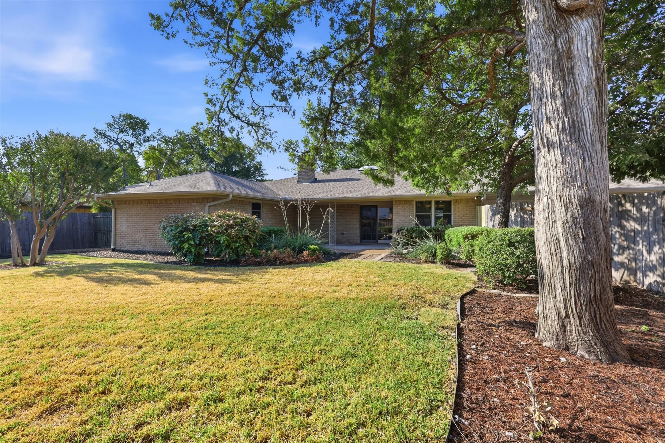 Brick exterior, gabled roofline, mature trees, landscaped planting beds, and wood privacy fencing
