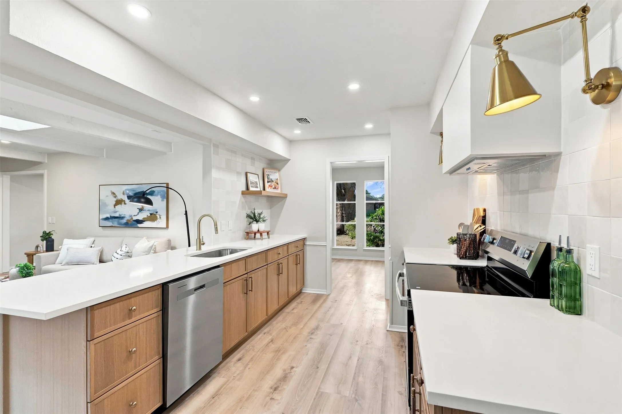 Contemporary kitchen featuring a stainless steel dishwasher, white countertops, wood-finish flooring, and recessed lighting