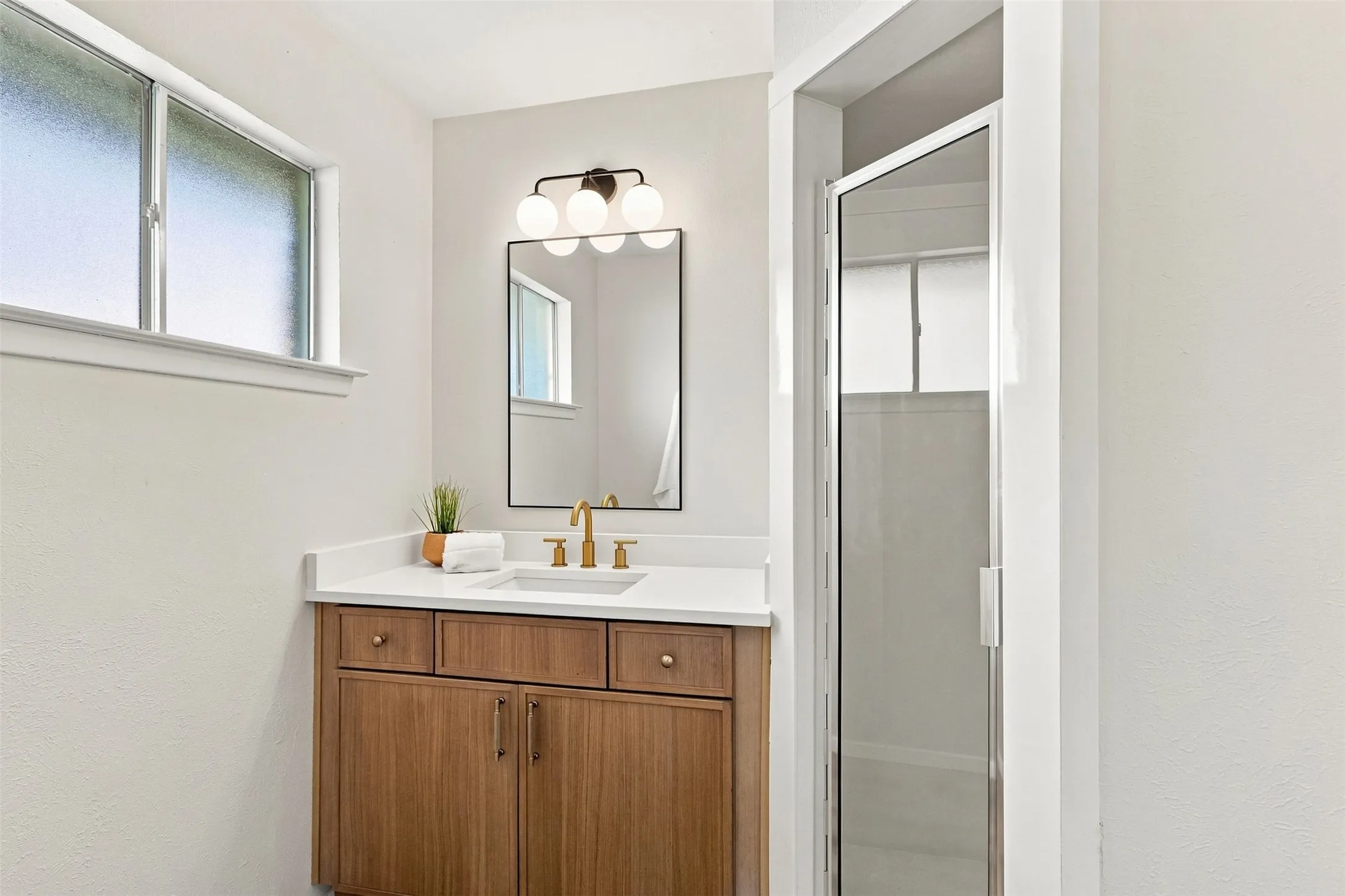 Wood-finish vanity with a white countertop and undermount sink, complemented by a rectangular mirror and a glass-enclosed shower