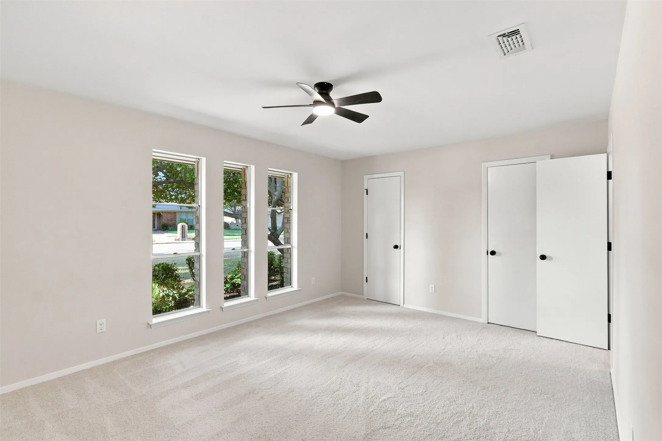 Carpeted room featuring multiple windows, a ceiling fan with light fixture, and closet doors