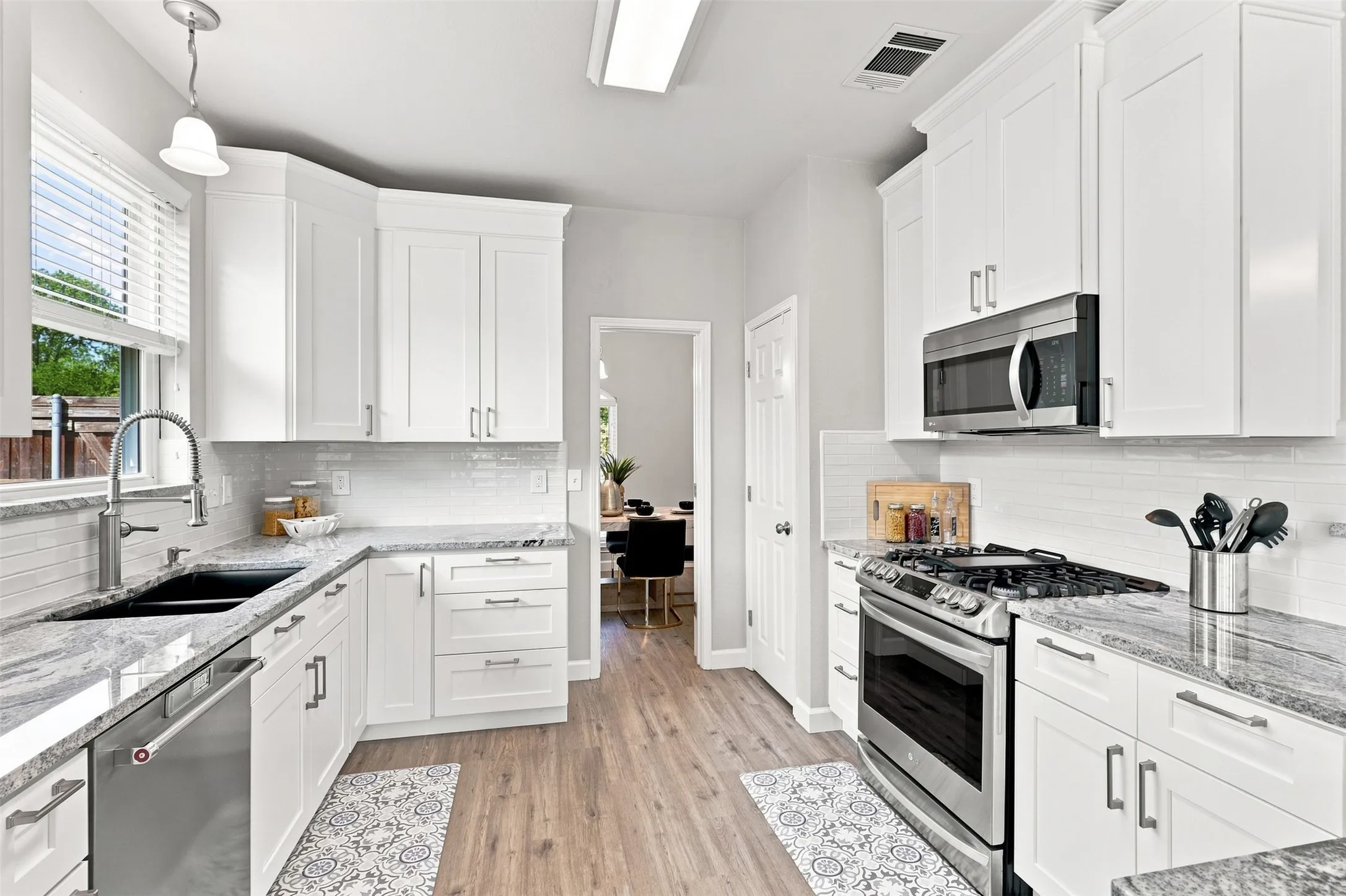 Modern kitchen featuring white shaker-style cabinetry, with soft touch cabinets stainless steel appliances, luxury vinyl plank flooring, granite countertops and coordinating white subway tile backsplash.