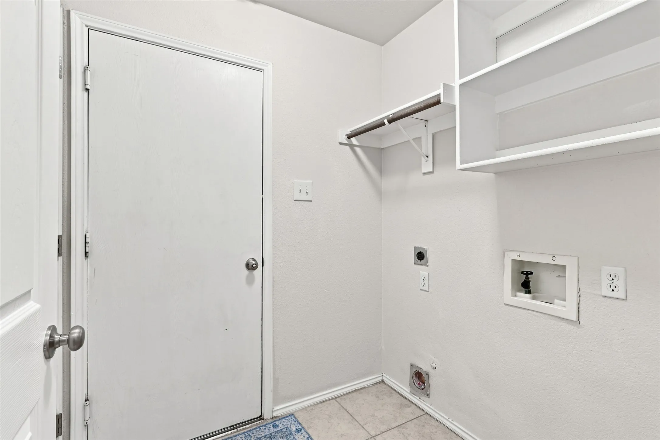 Utility room featuring tile flooring, built-in shelving, and a clothes hanging rod.