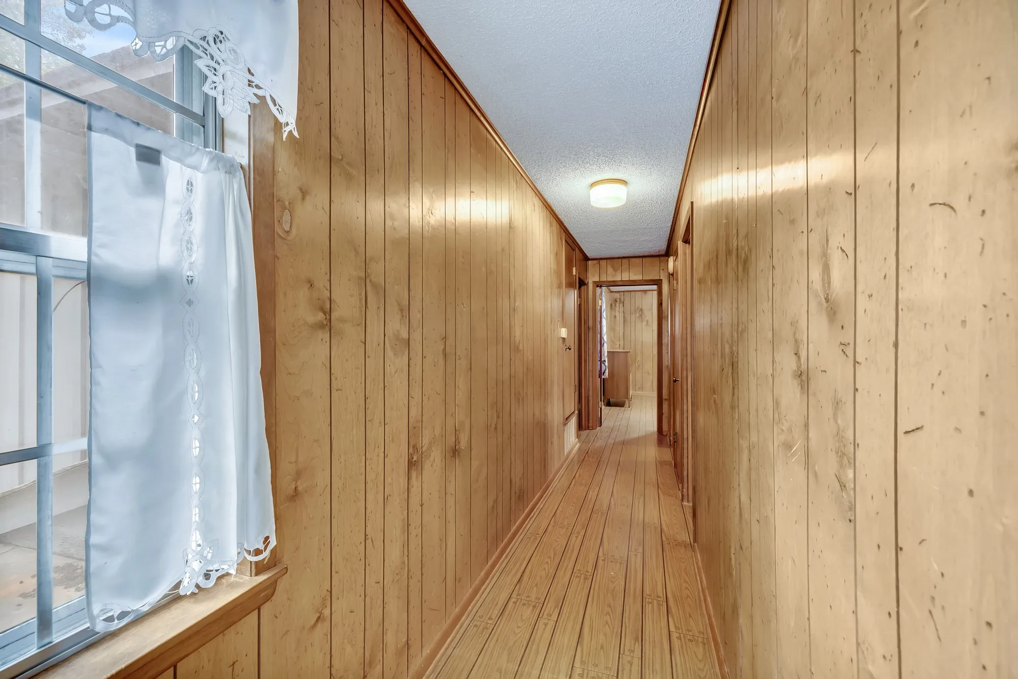 Wood-finish flooring and wall paneling in a hallway with a flush-mount ceiling light
