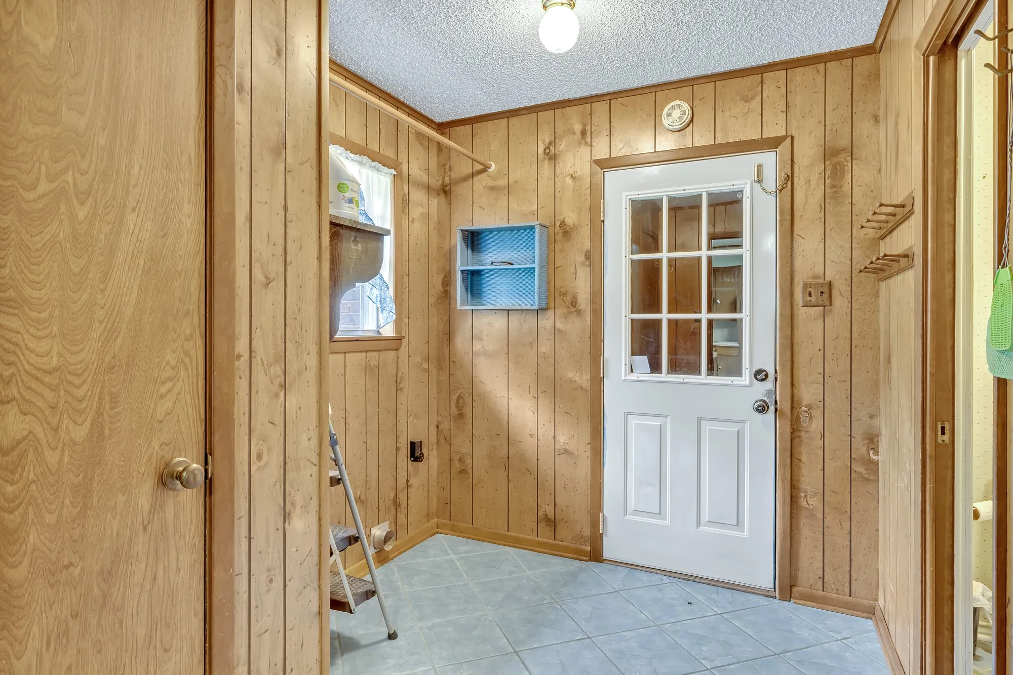 Wood-paneled walls, tiled flooring, white paneled door with glass inserts, built-in shelving, and a small window