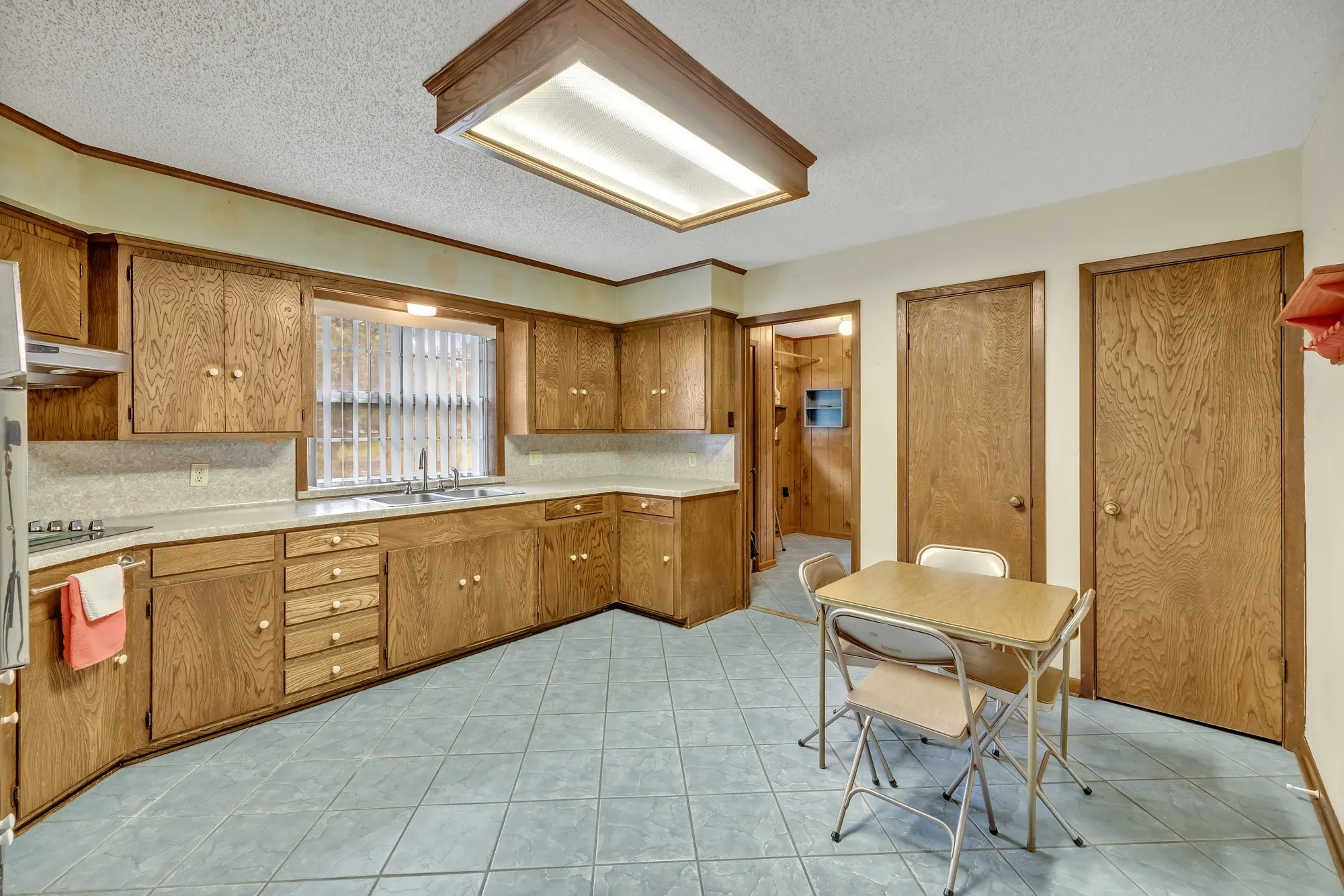 Full kitchen with wood-finish cabinetry, tile flooring, and a window with a sink