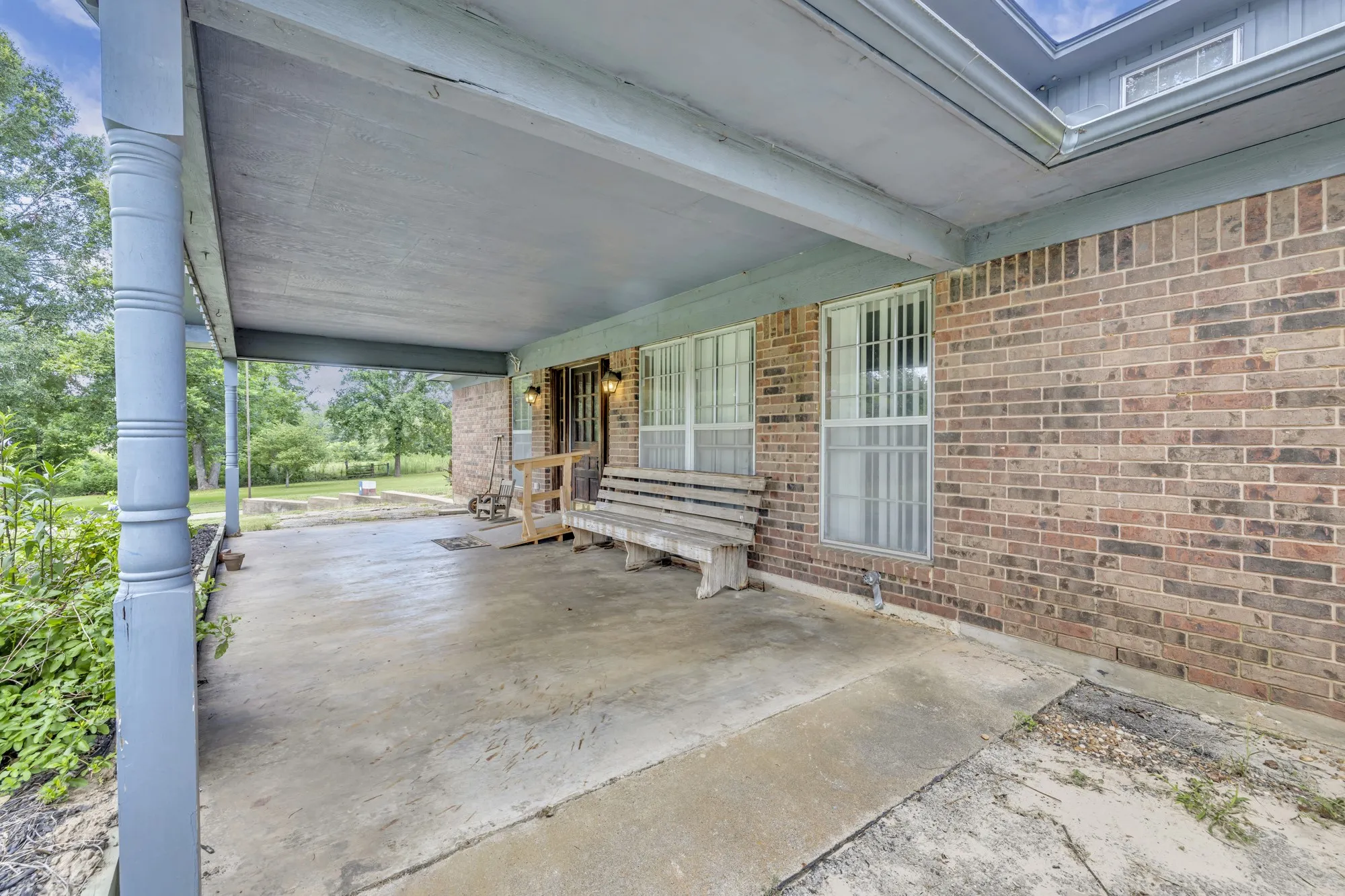 Covered front porch with a concrete surface, brick exterior, and multiple windows
