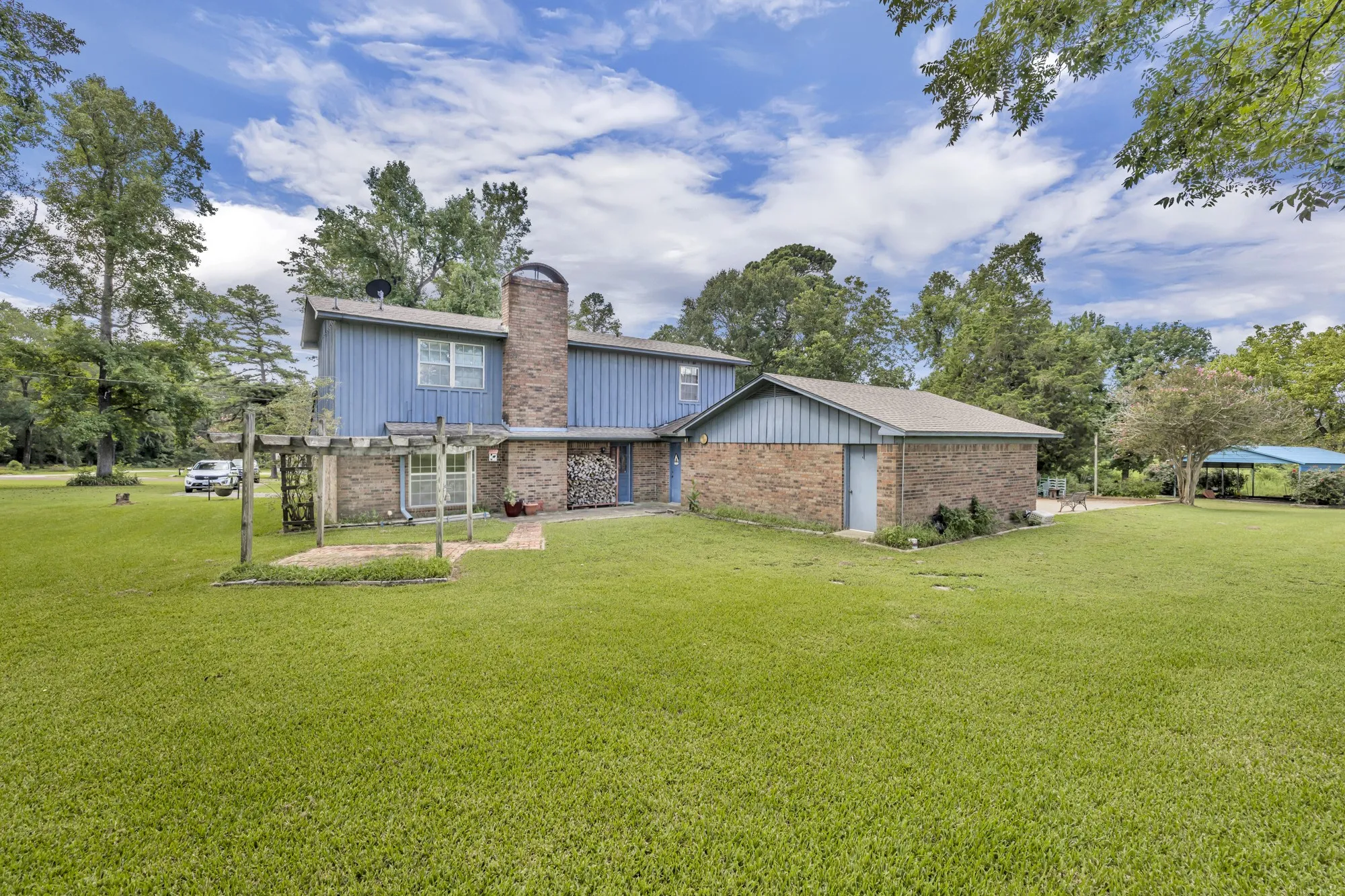 Expansive green lawn surrounds the property, featuring a brick and siding exterior, a prominent brick chimney, and an attached structure with a pitched roof