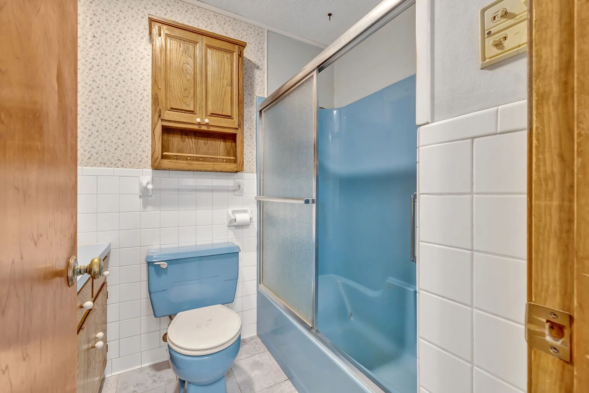 Bathroom featuring a blue bathtub and toilet, white tile walls, and a wood-finish cabinet
