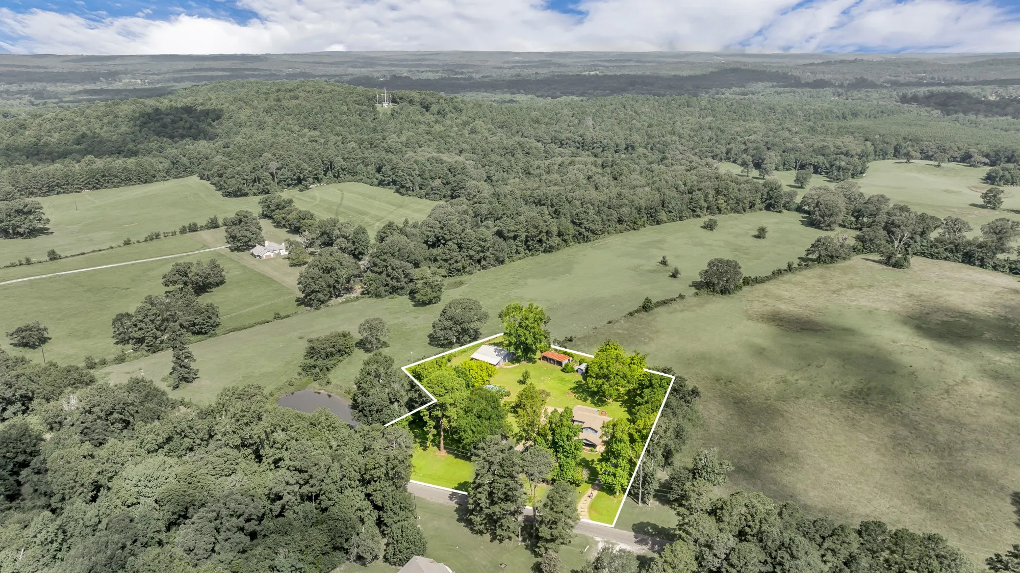 Expansive rural property featuring a primary residence, a detached structure, and a pond
