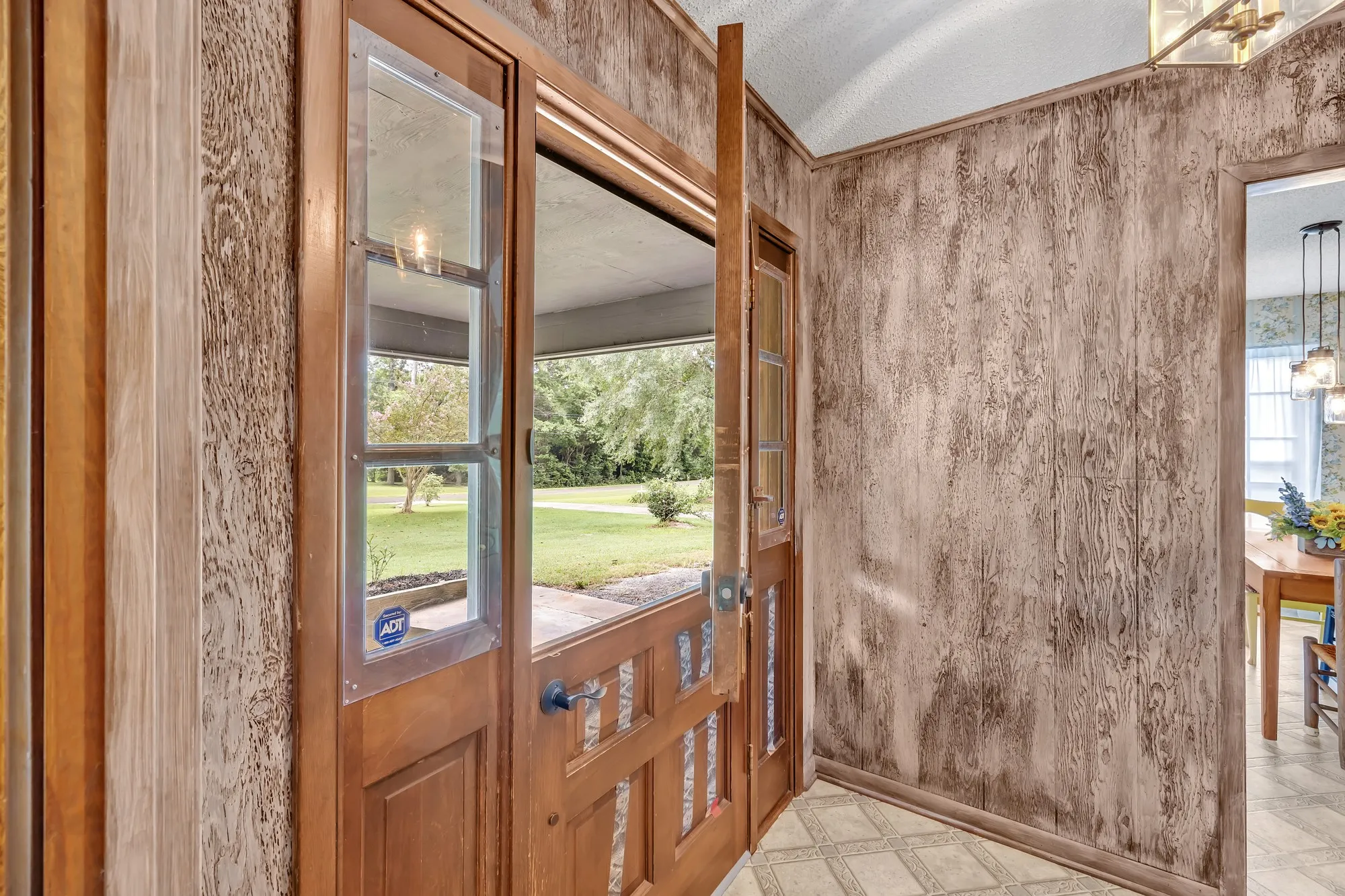 Wood-paneled wall, full-light wood-frame entry door, patterned flooring, and a brass-finish chandelier