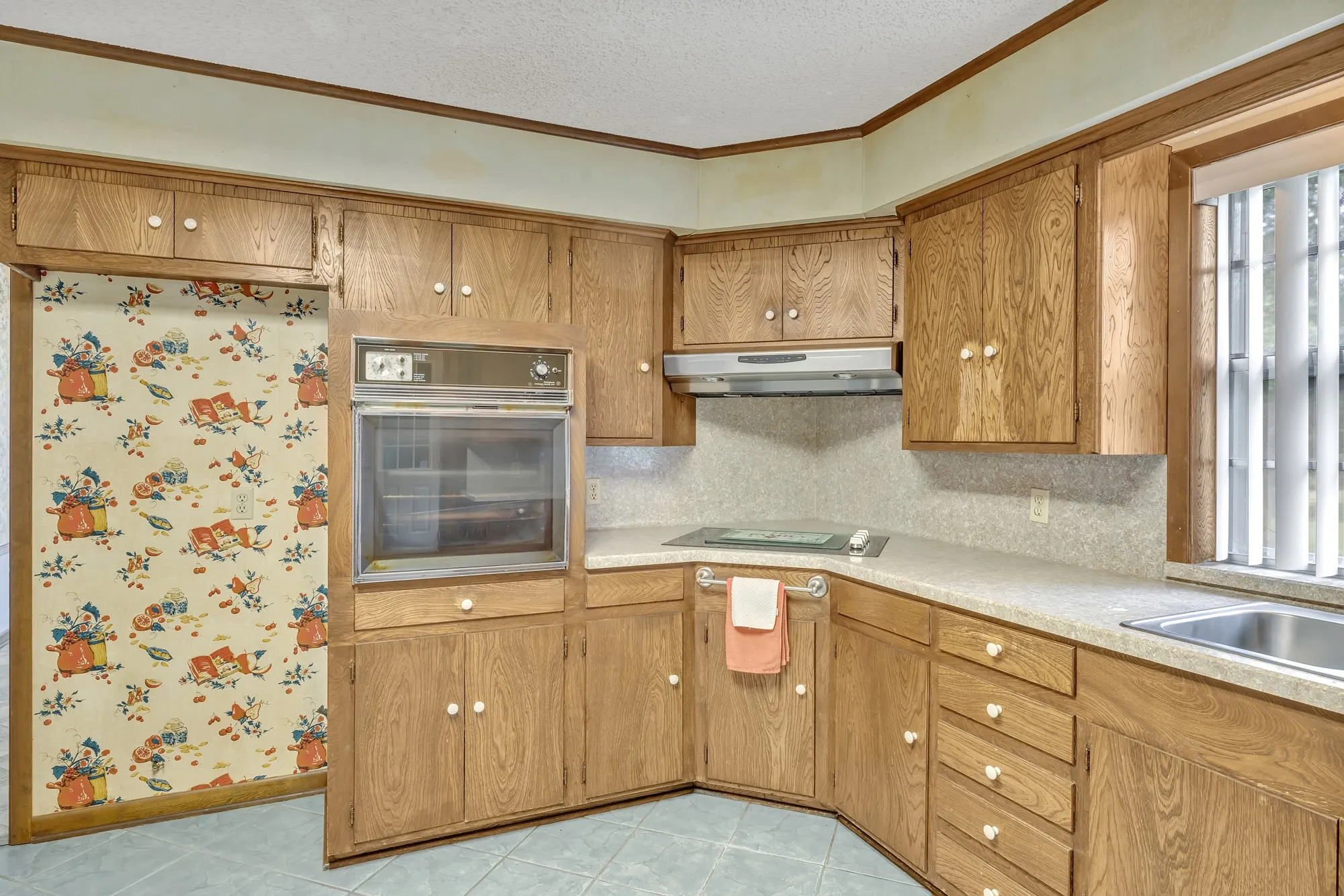 Kitchen featuring wood-finish cabinetry, built-in wall oven, built-in cooktop, stainless steel sink, and light-toned countertops