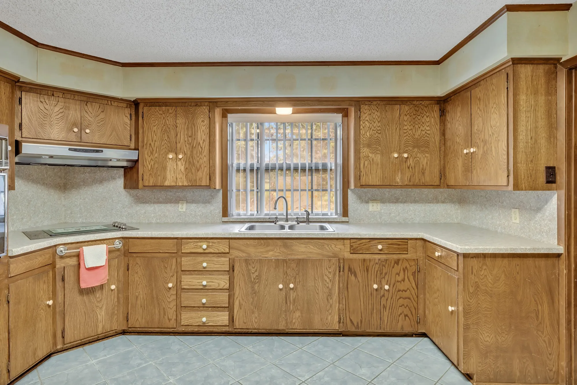 Spacious kitchen featuring warm wood cabinetry with ample storage, tile flooring, stainless steel appliances, and a large window above the sink providing natural light