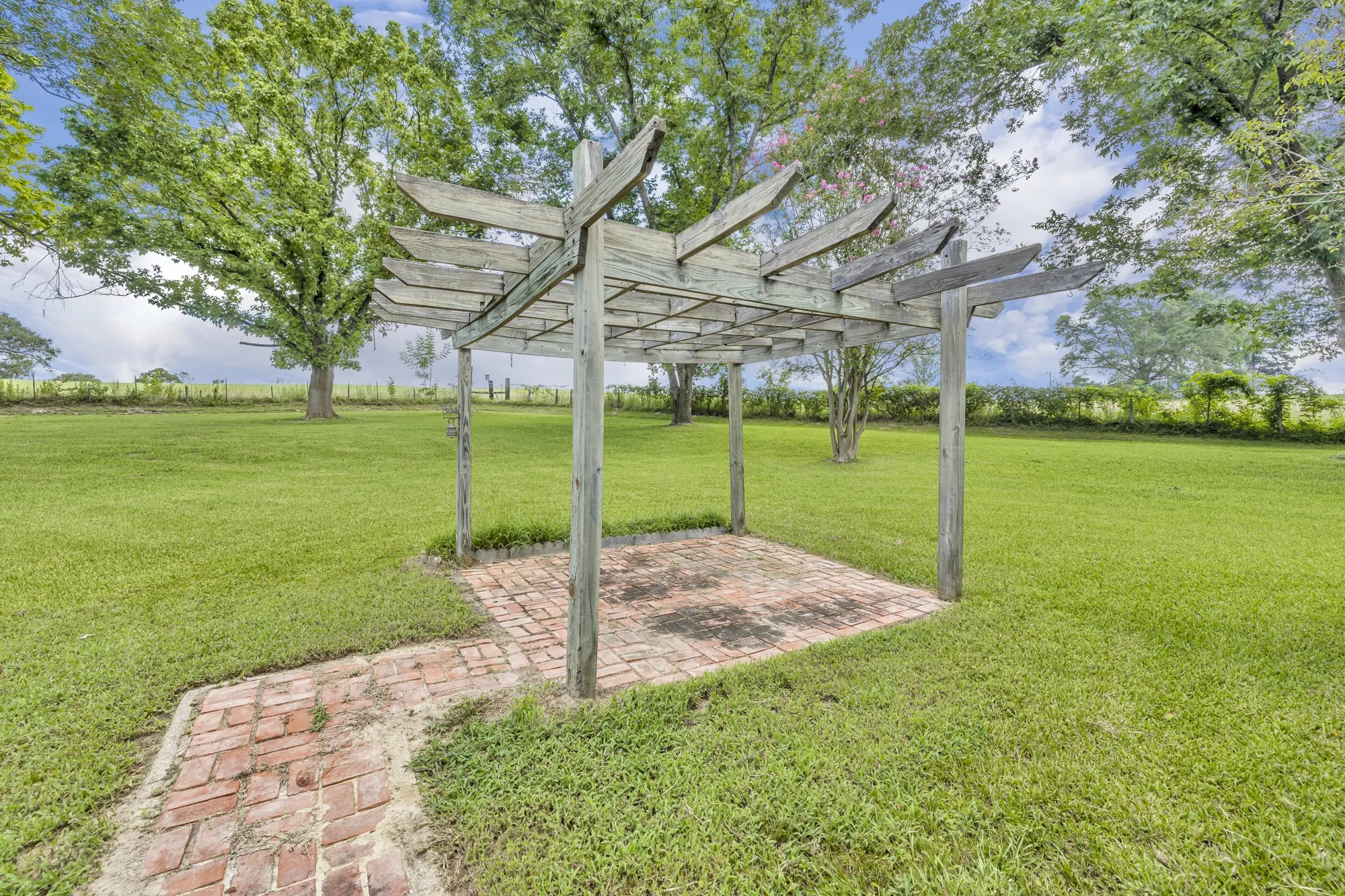 Expansive manicured lawn with mature shade trees and a wood-finish pergola featuring lattice overhead panels