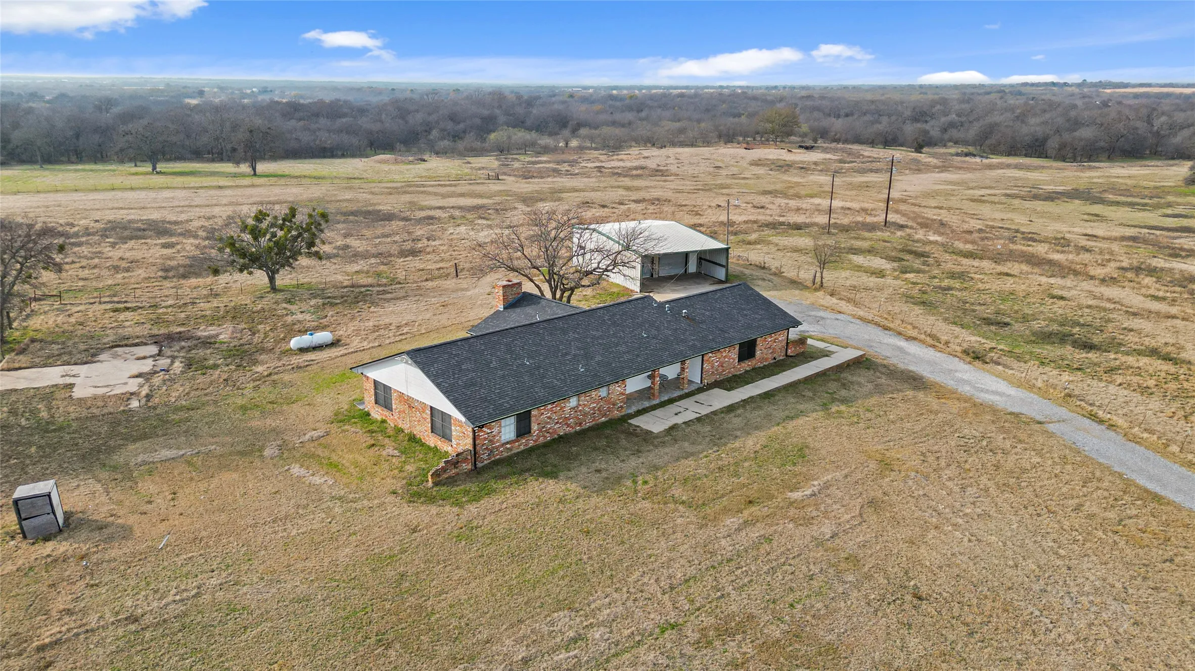 Brick exterior, dark shingle roof, attached covered porch, detached metal outbuilding, paved driveway