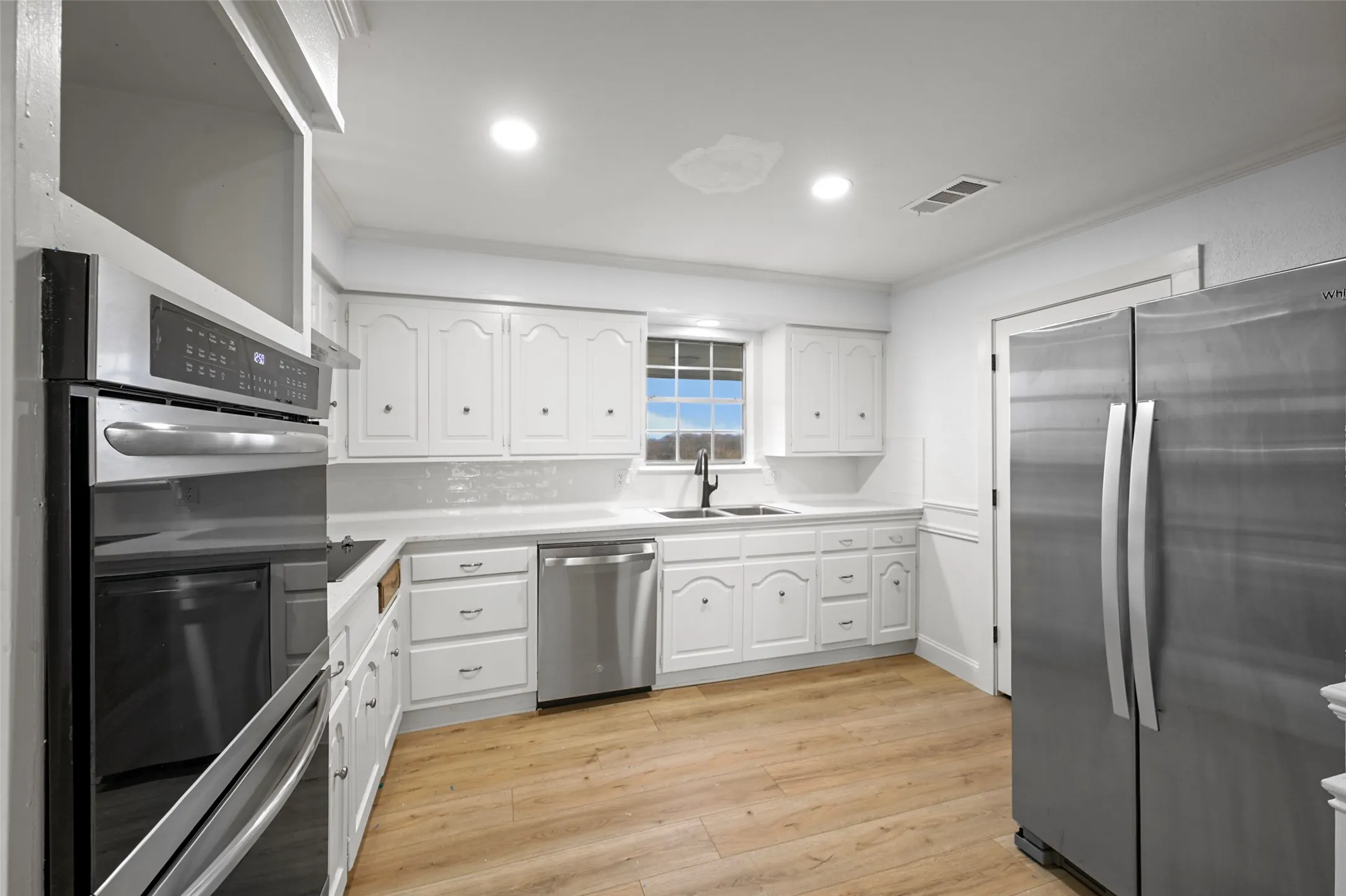 Kitchen featuring white cabinetry, light countertops, wood-finish flooring, stainless steel appliances, and a window