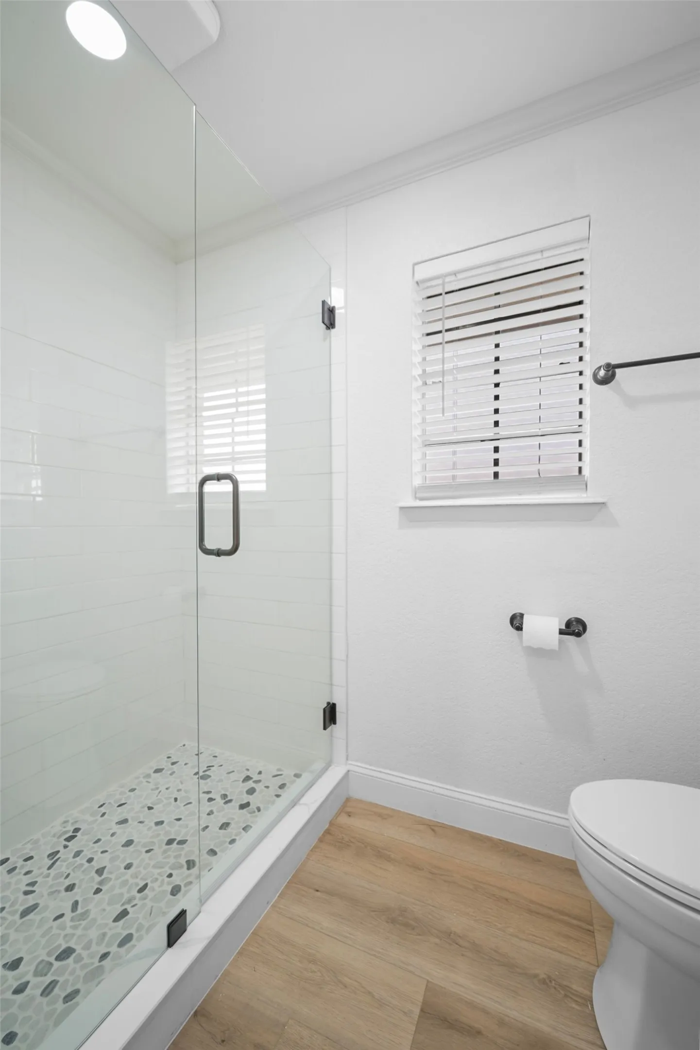 Glass-enclosed shower with pebble-tile flooring, white subway tile surround, wood-finish flooring, and crown molding