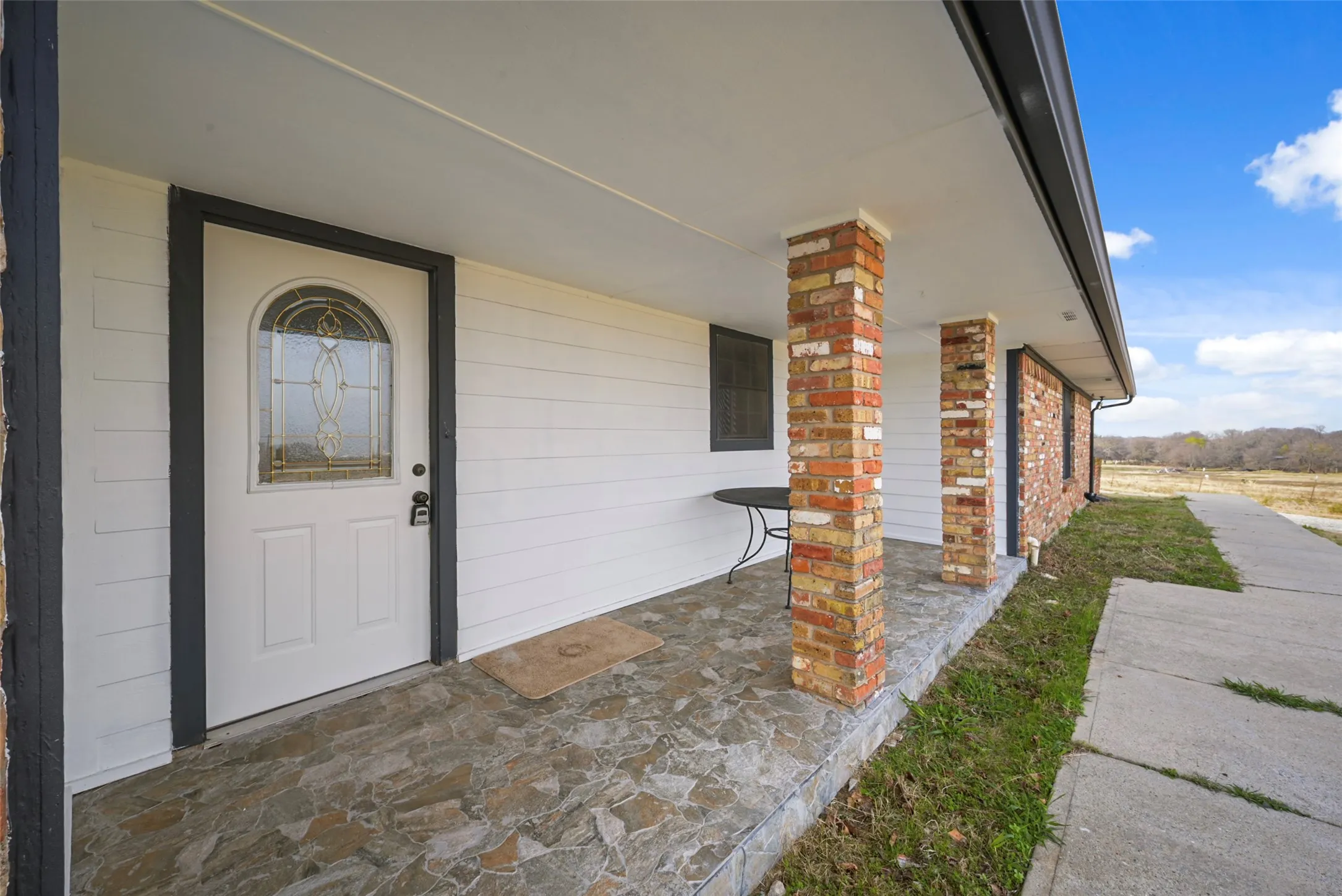 Covered front entry with a decorative glass door, brick columns, and a stone-finish porch