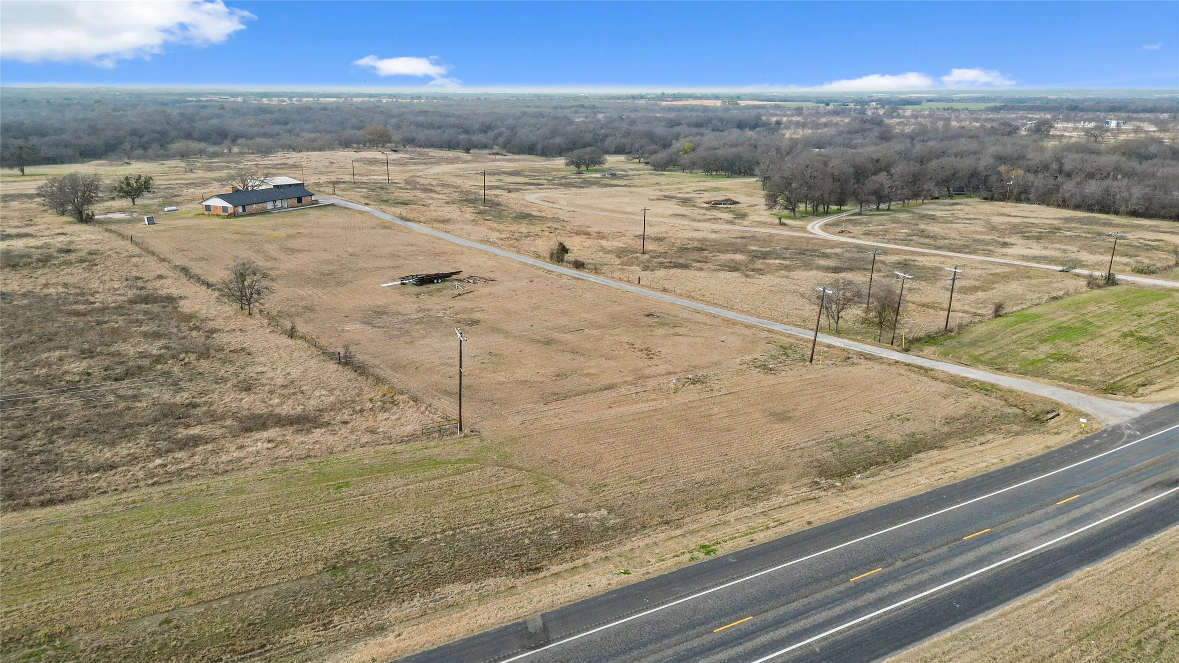 Expansive undeveloped land with a distant structure, bordered by a paved road and natural tree lines